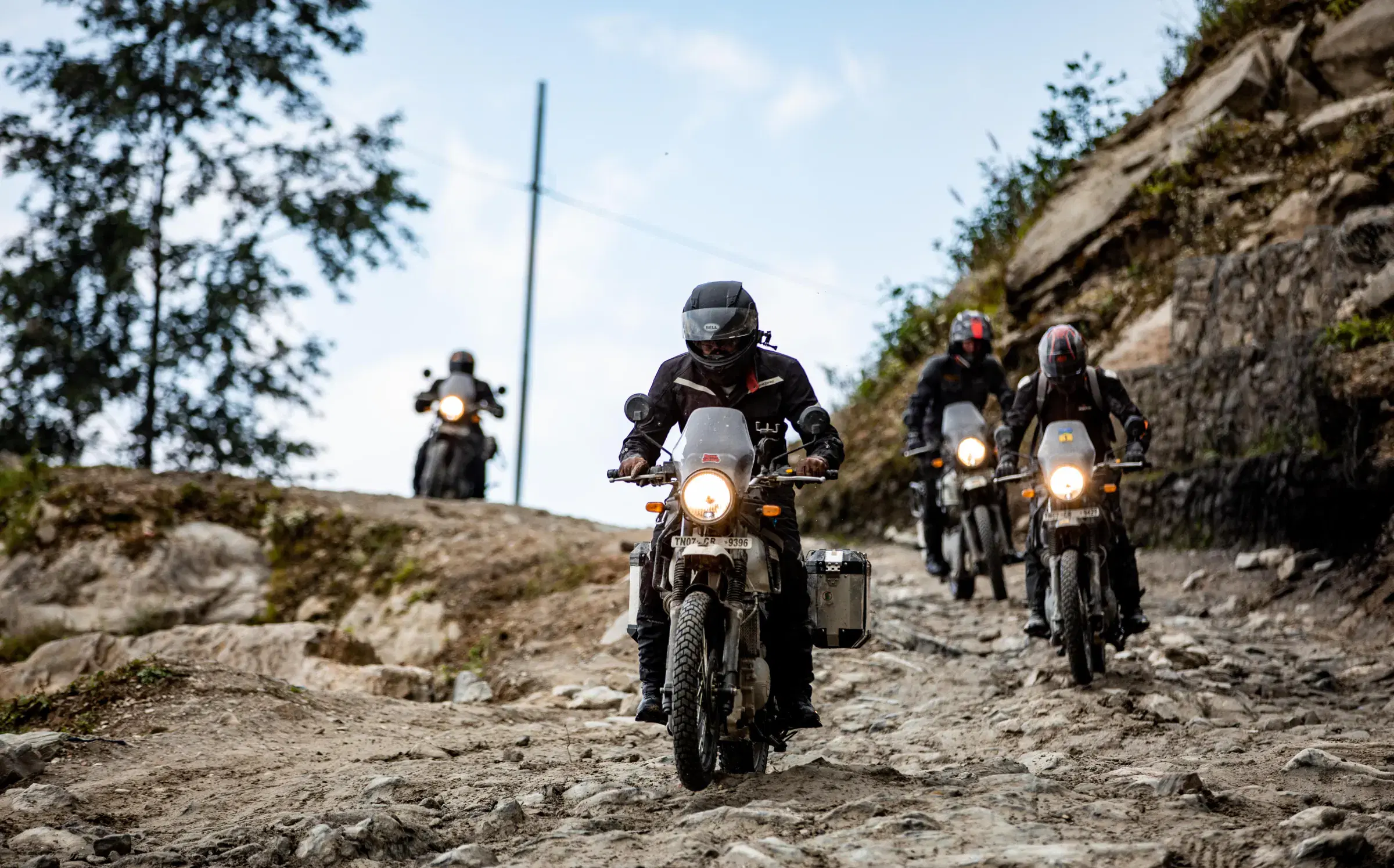 Outdoor adventure scene featuring people, a vehicle, rocky terrain, a built structure, and blue sky.
