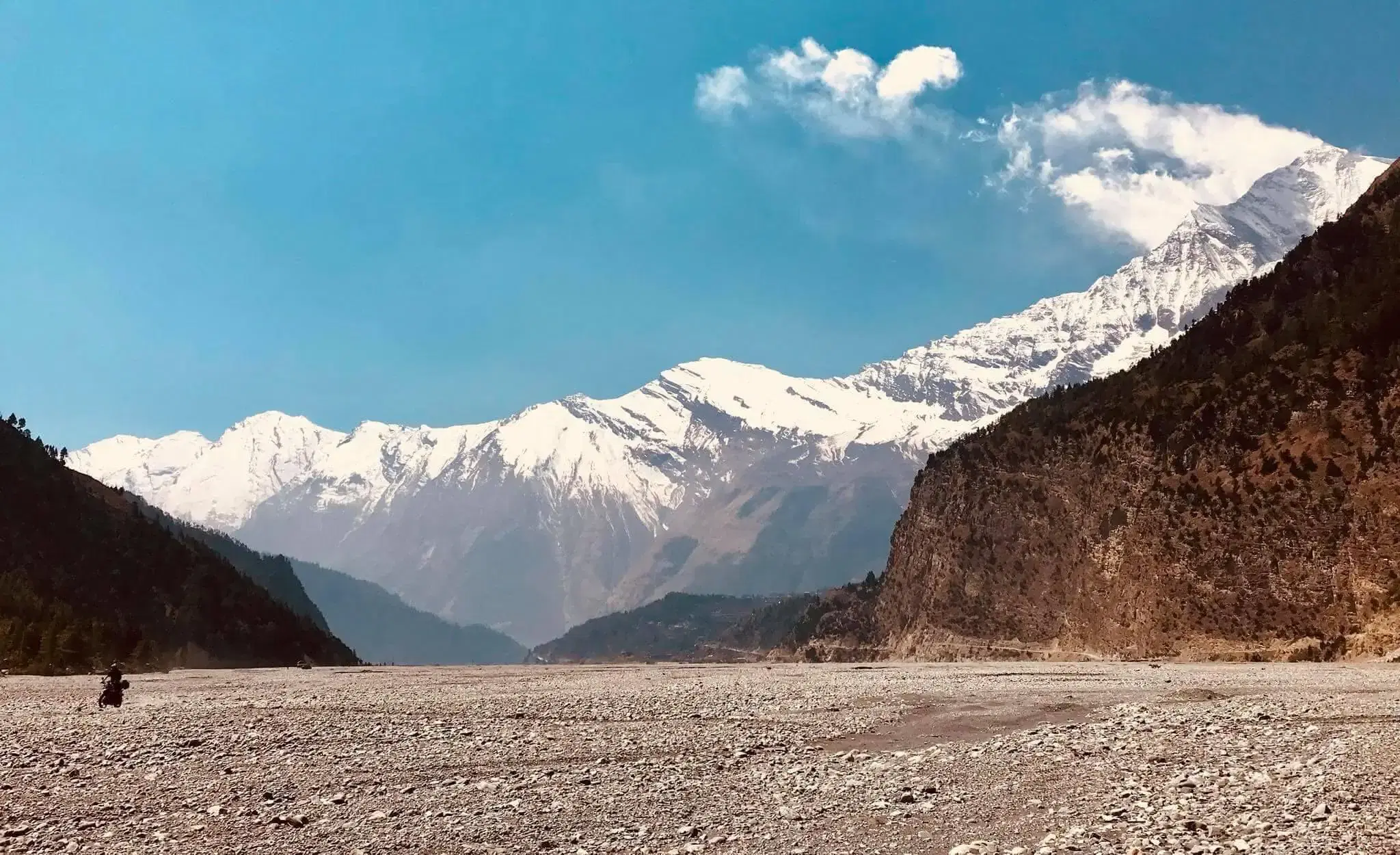Mountain landscape featuring snowy terrain, water, and cloudy sky.