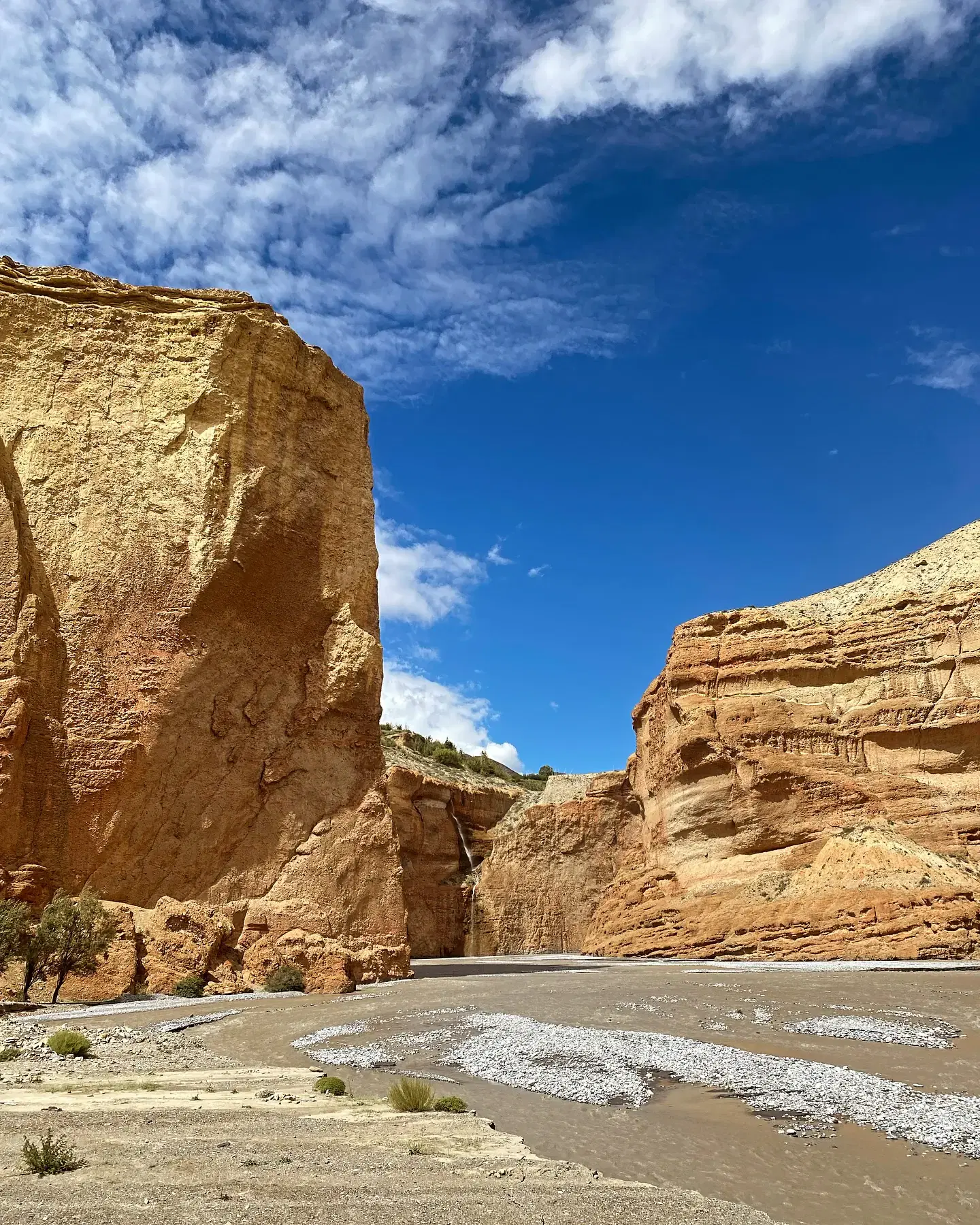 Portrait-oriented Mountain landscape featuring rocky terrain, a built structure, and cloudy sky.