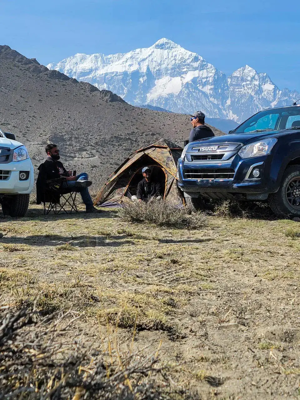 Portrait-oriented Outdoor adventure scene featuring people, a vehicle, rocky terrain, blue sky, and greenery.
