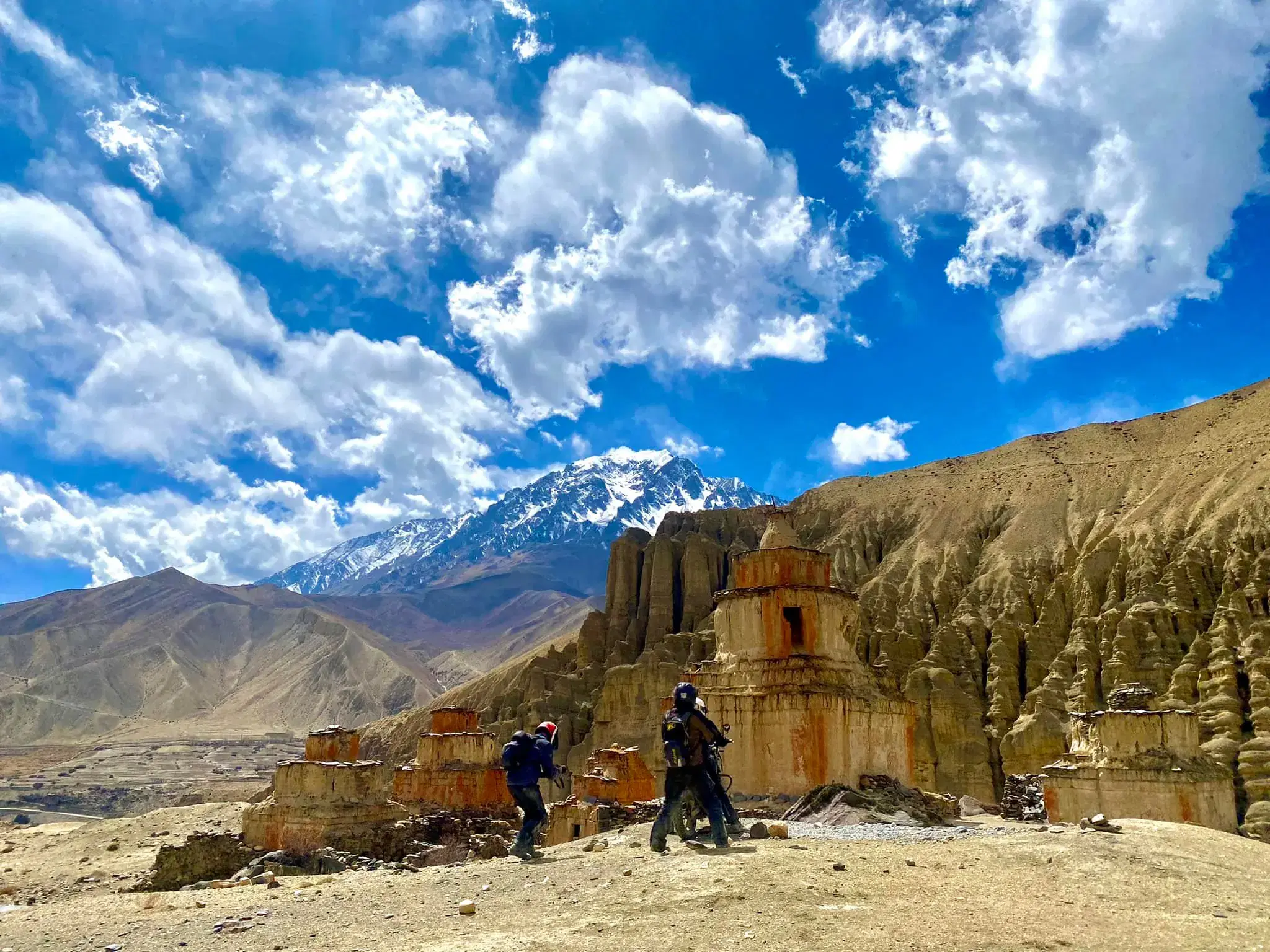 Outdoor scene featuring people, rocky terrain, a built structure, and cloudy sky.