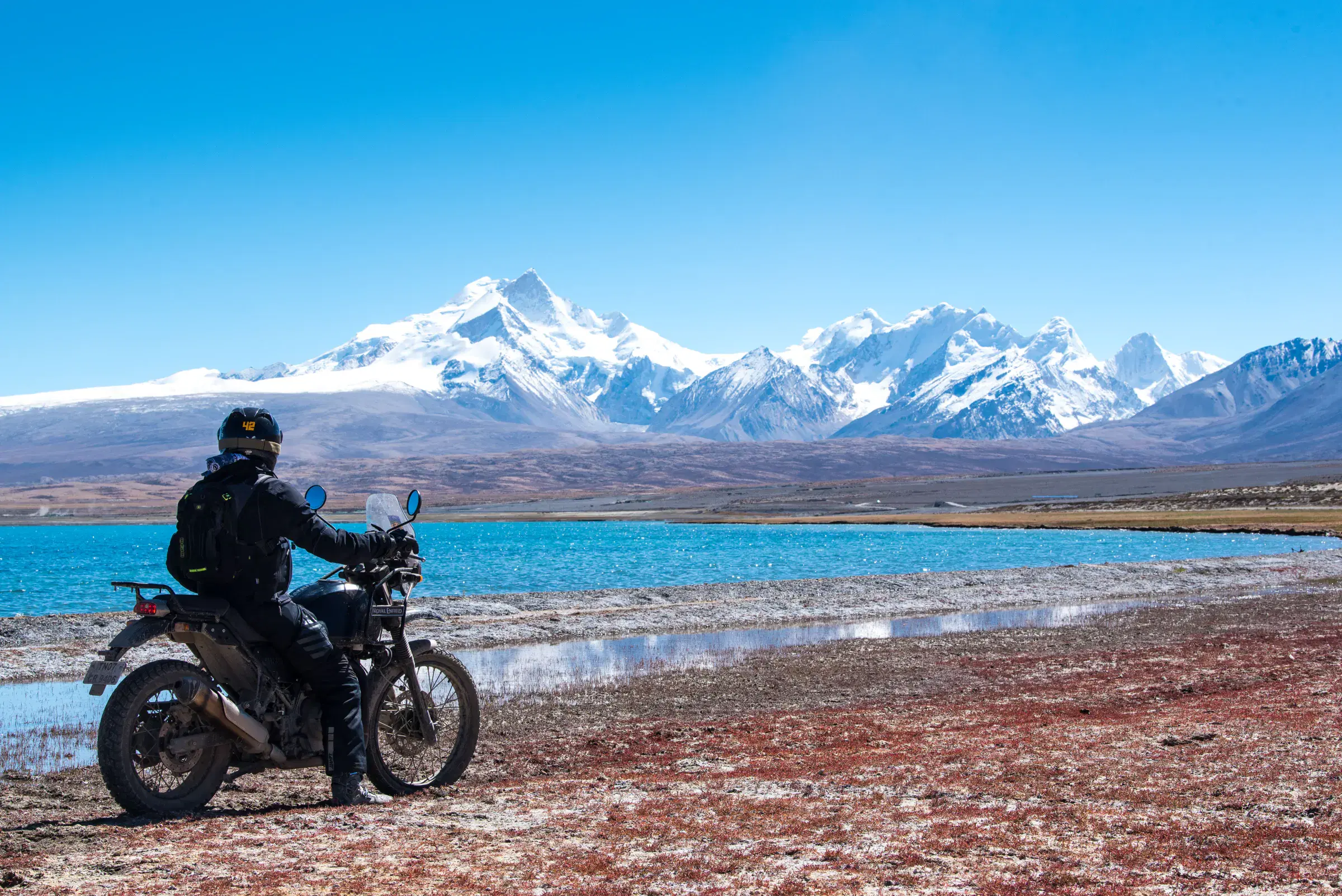 Outdoor scene featuring people, snowy terrain, water, and blue sky.