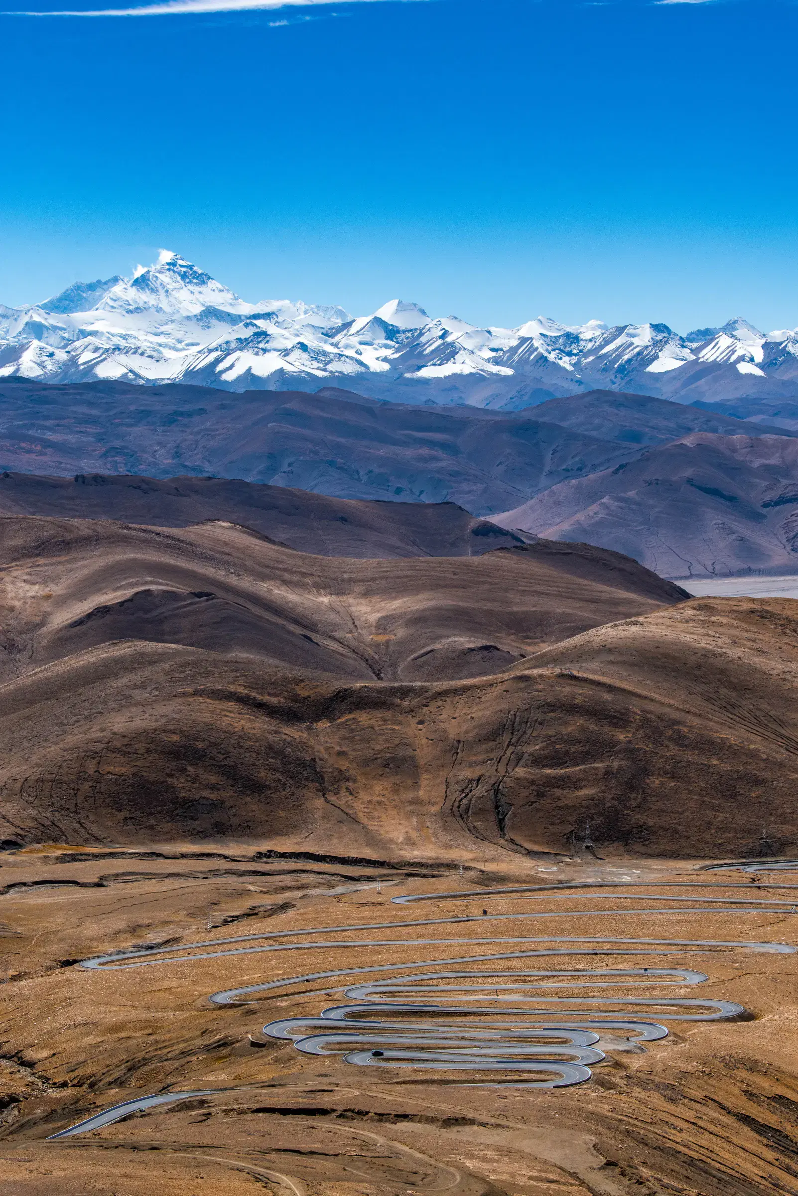 Portrait-oriented Mountain landscape featuring snowy terrain, water, and blue sky.
