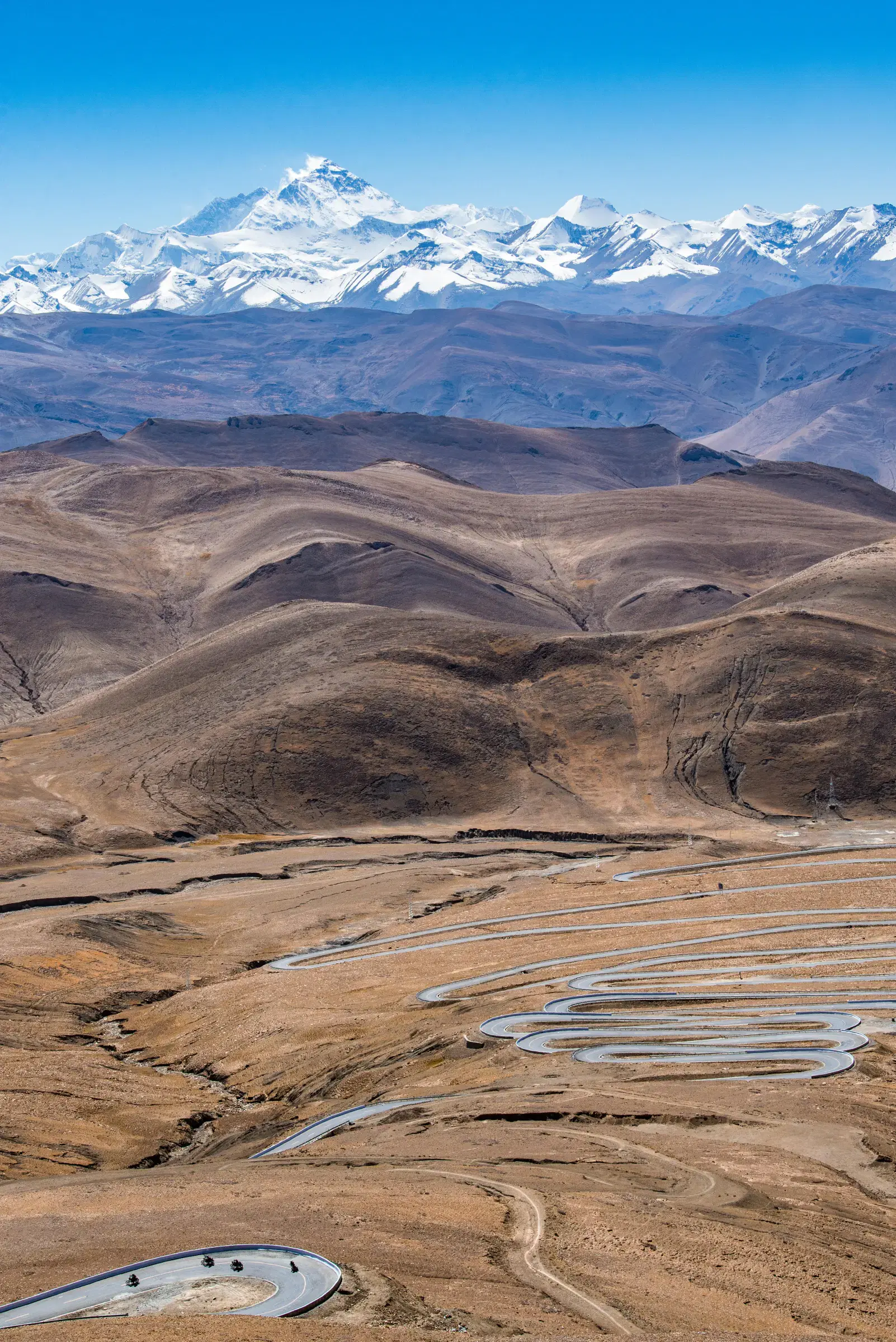 Portrait-oriented Mountain landscape featuring snowy terrain, water, and blue sky.