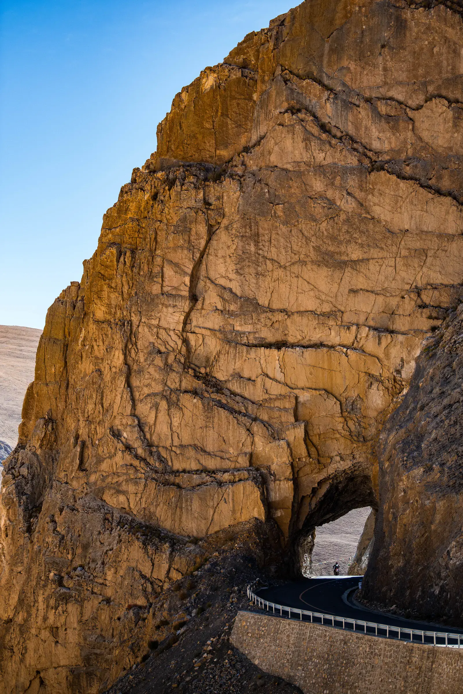 Portrait-oriented Mountain landscape featuring rocky terrain, a built structure, and blue sky.