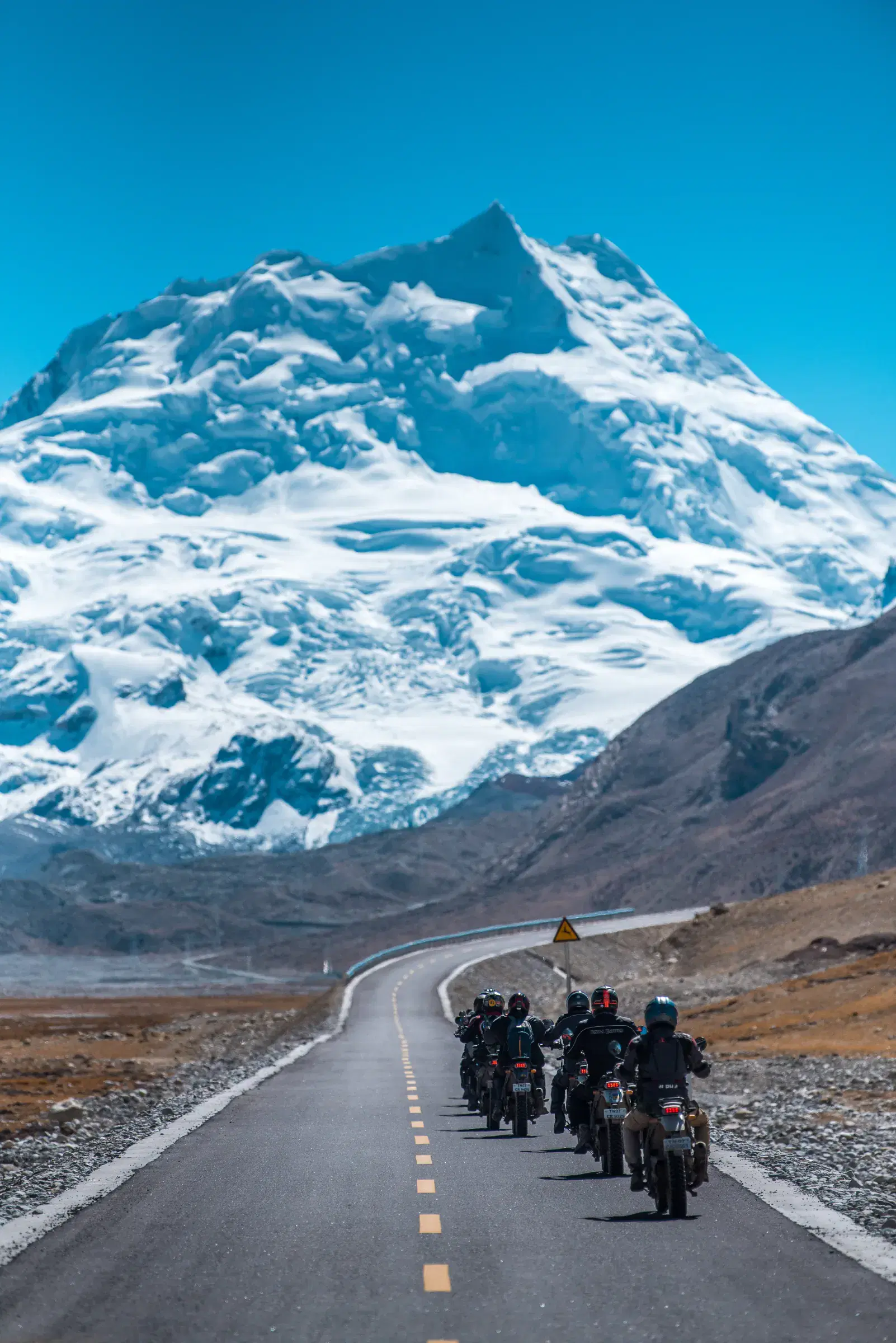 Portrait-oriented Mountain landscape featuring snowy terrain, water, and blue sky.