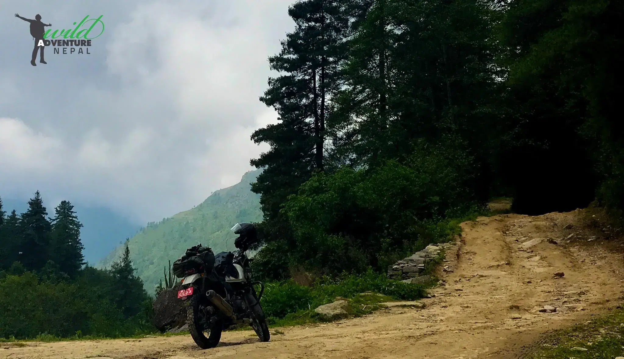 Outdoor scene featuring people, rocky terrain, a built structure, and cloudy sky.