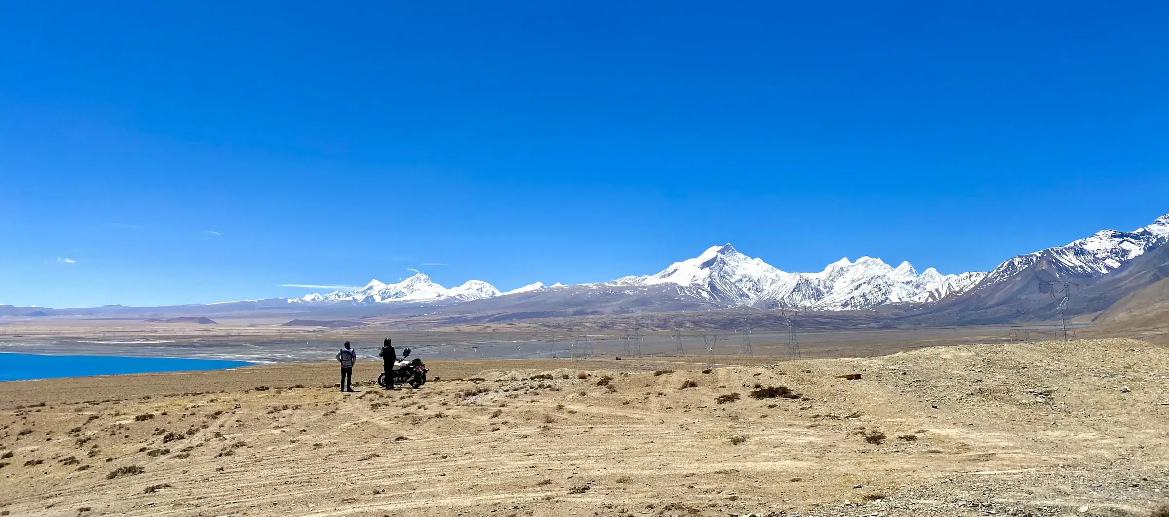 Panoramic Outdoor scene featuring people, snowy terrain, and blue sky.