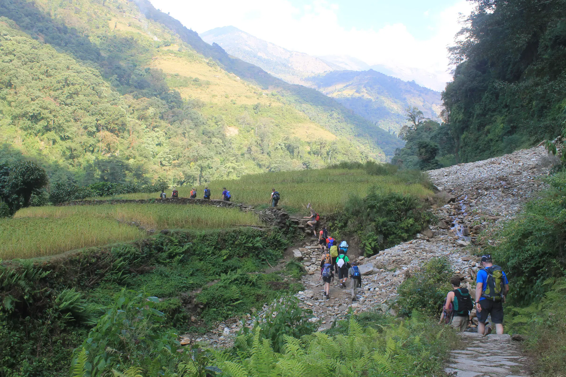 Outdoor scene featuring people, rocky terrain, a built structure, and cloudy sky.