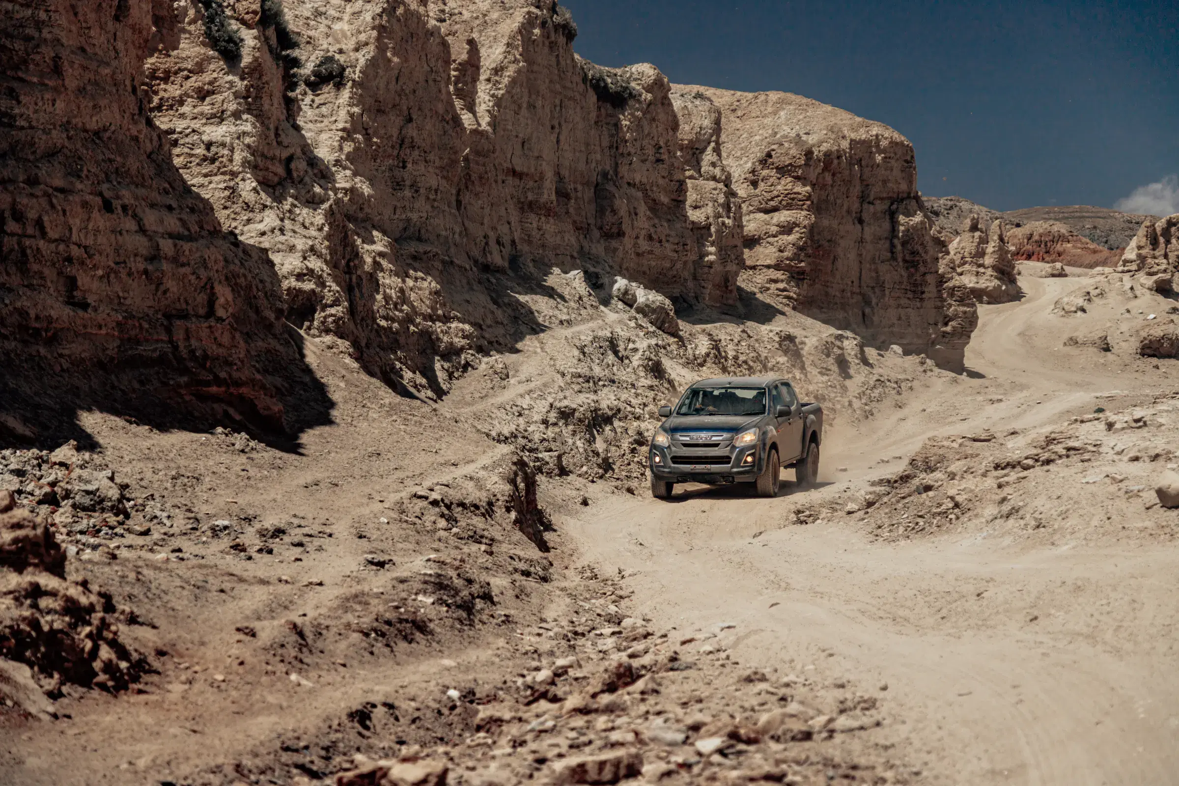 Outdoor vehicle scene featuring a vehicle, rocky terrain, a built structure, and blue sky.