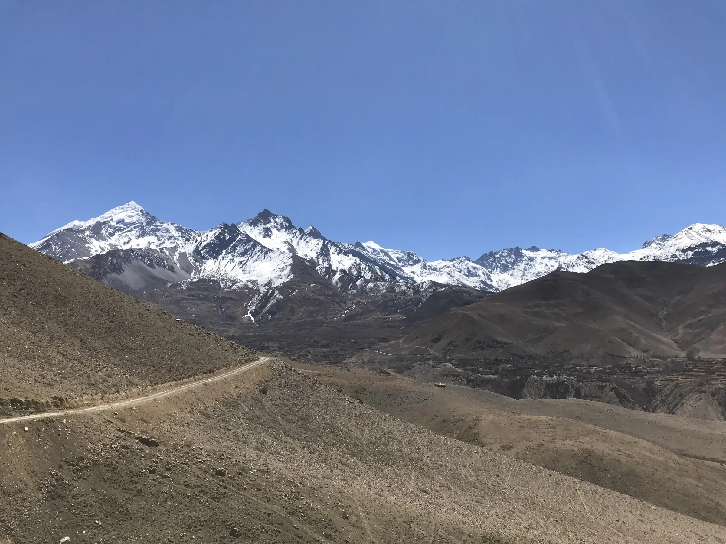 Mountain landscape featuring snowy terrain, water, and blue sky.