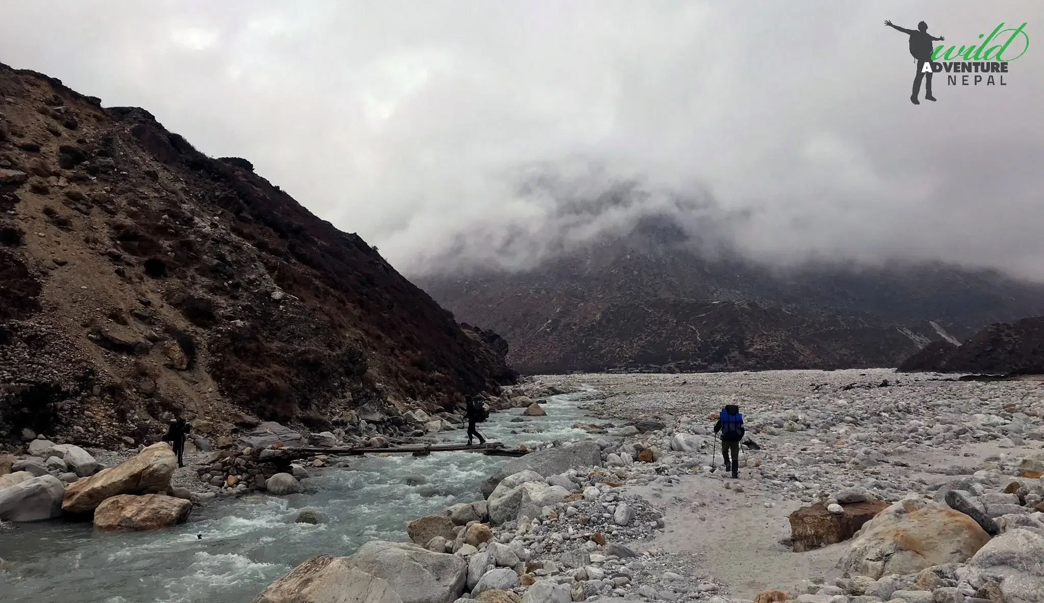 Outdoor scene featuring people, rocky terrain, a built structure, and cloudy sky.