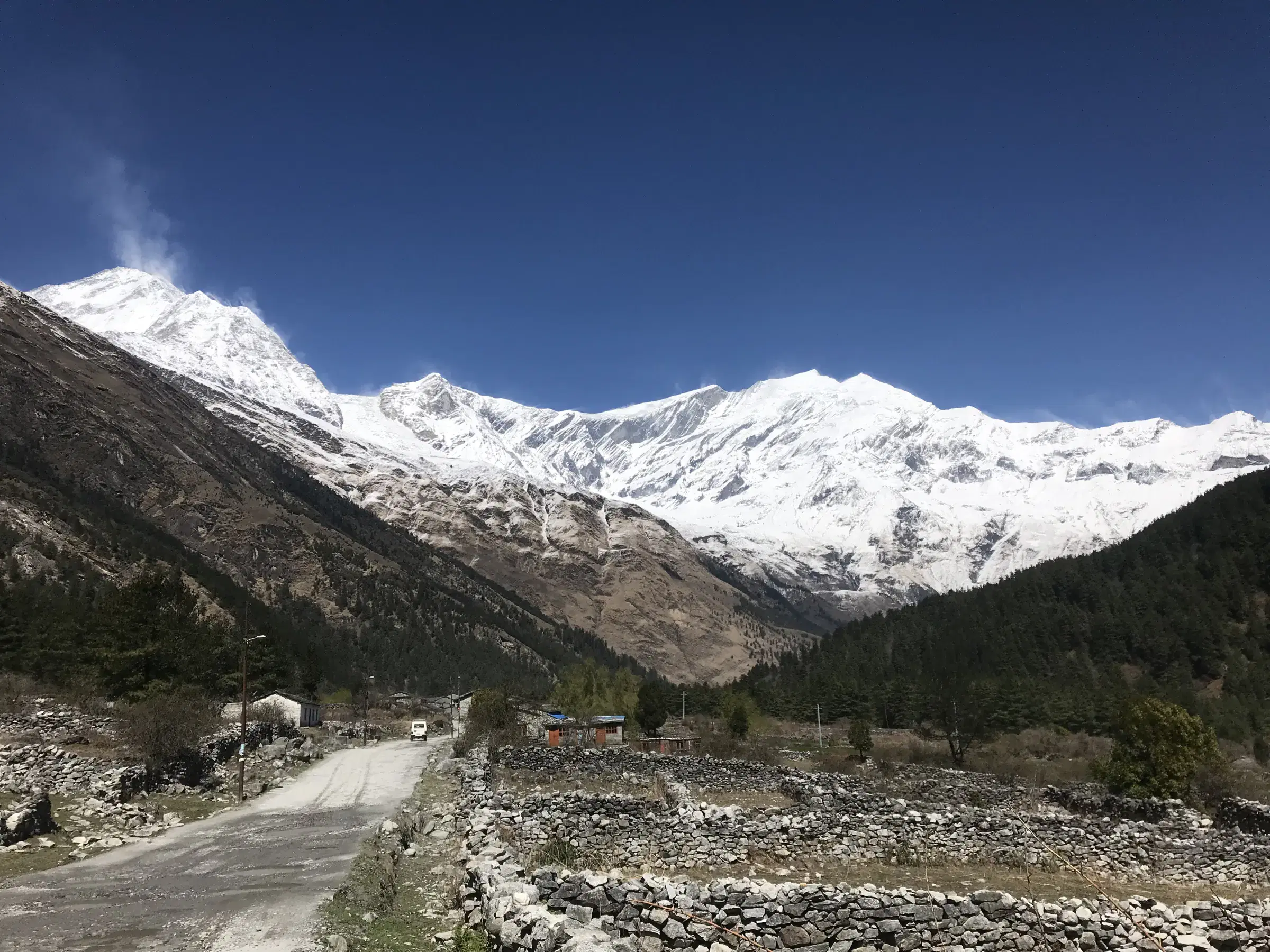 Mountain landscape featuring snowy terrain, water, a built structure, and blue sky.