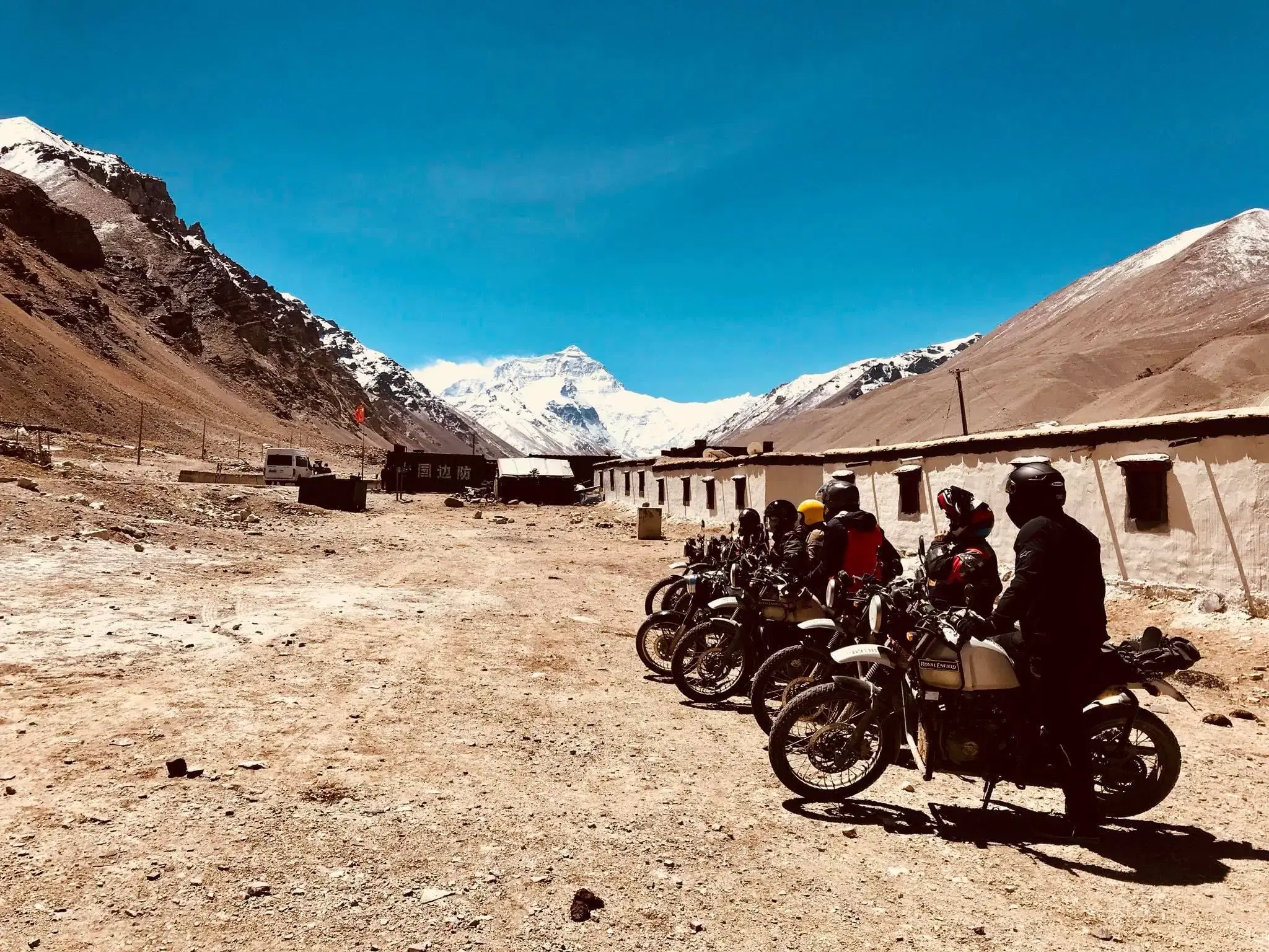 Outdoor scene featuring people, rocky terrain, a built structure, and blue sky.