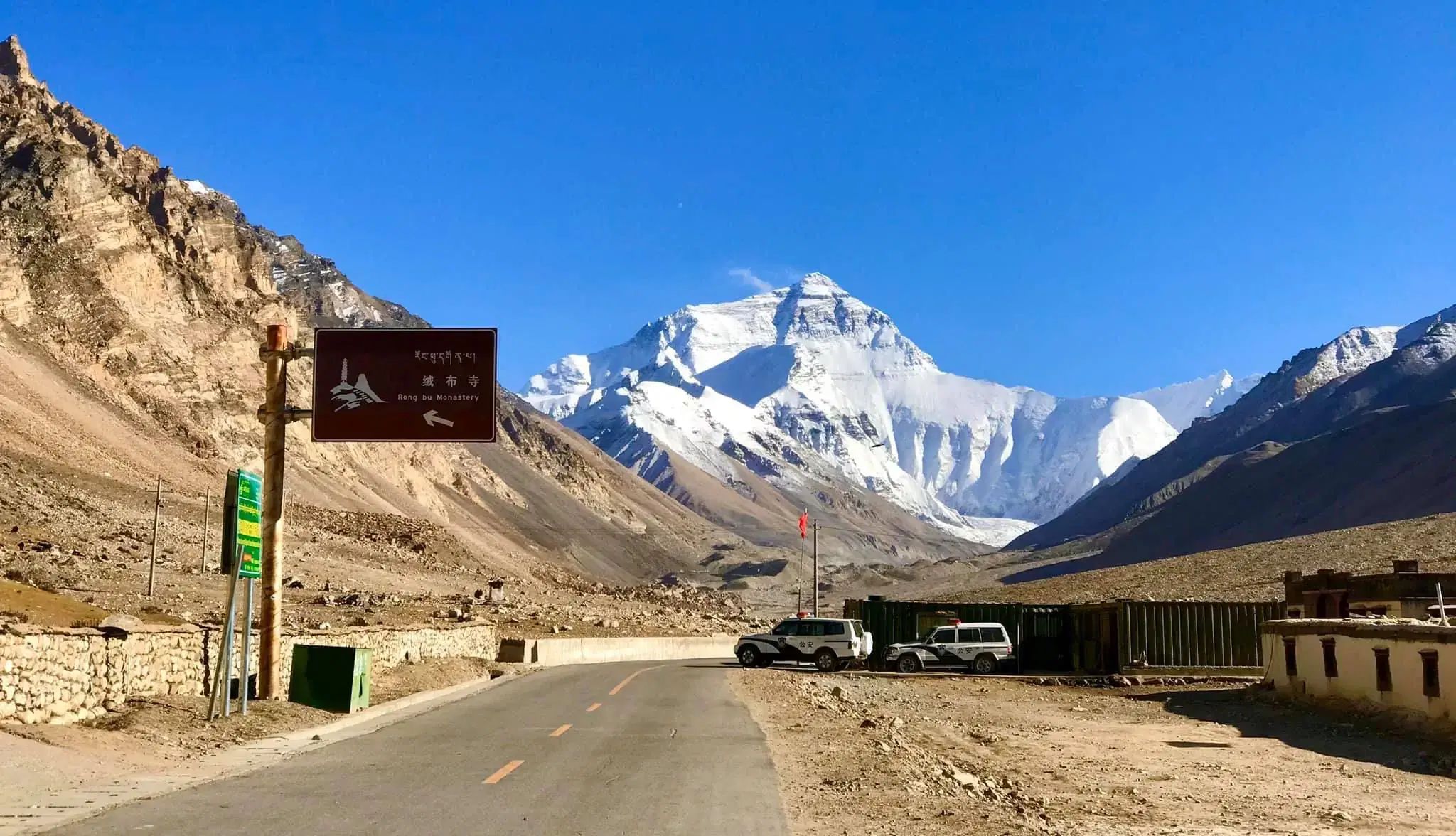 Mountain landscape featuring snowy terrain, water, a built structure, and blue sky.