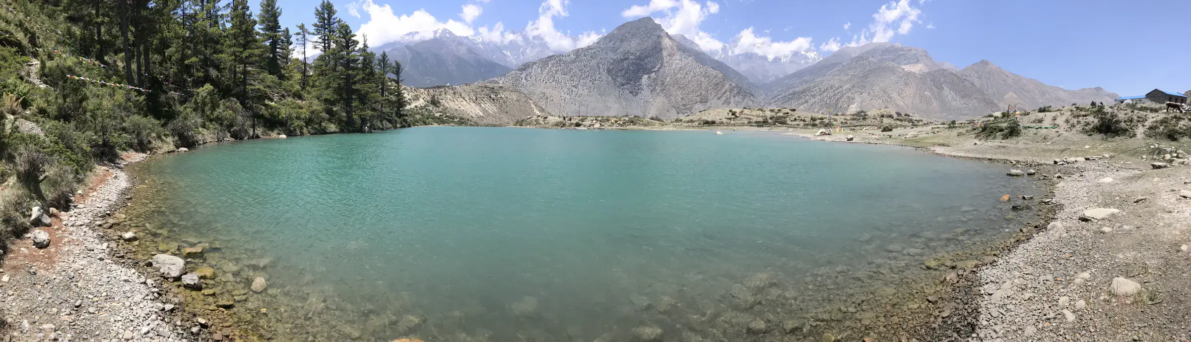 Panoramic Mountain landscape featuring rocky terrain, water, a built structure, and cloudy sky.
