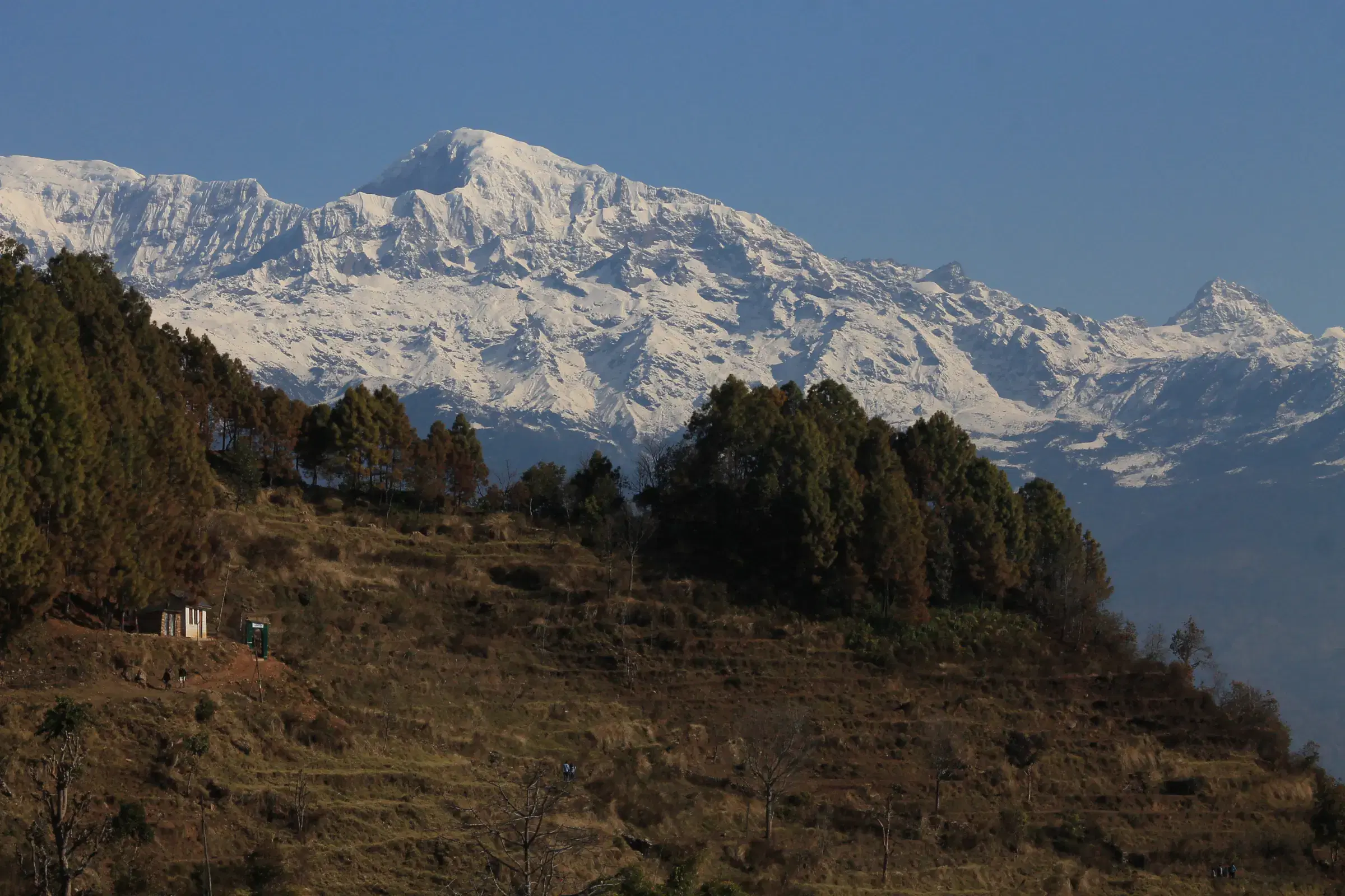 Mountain landscape featuring snowy terrain, water, blue sky, and greenery.