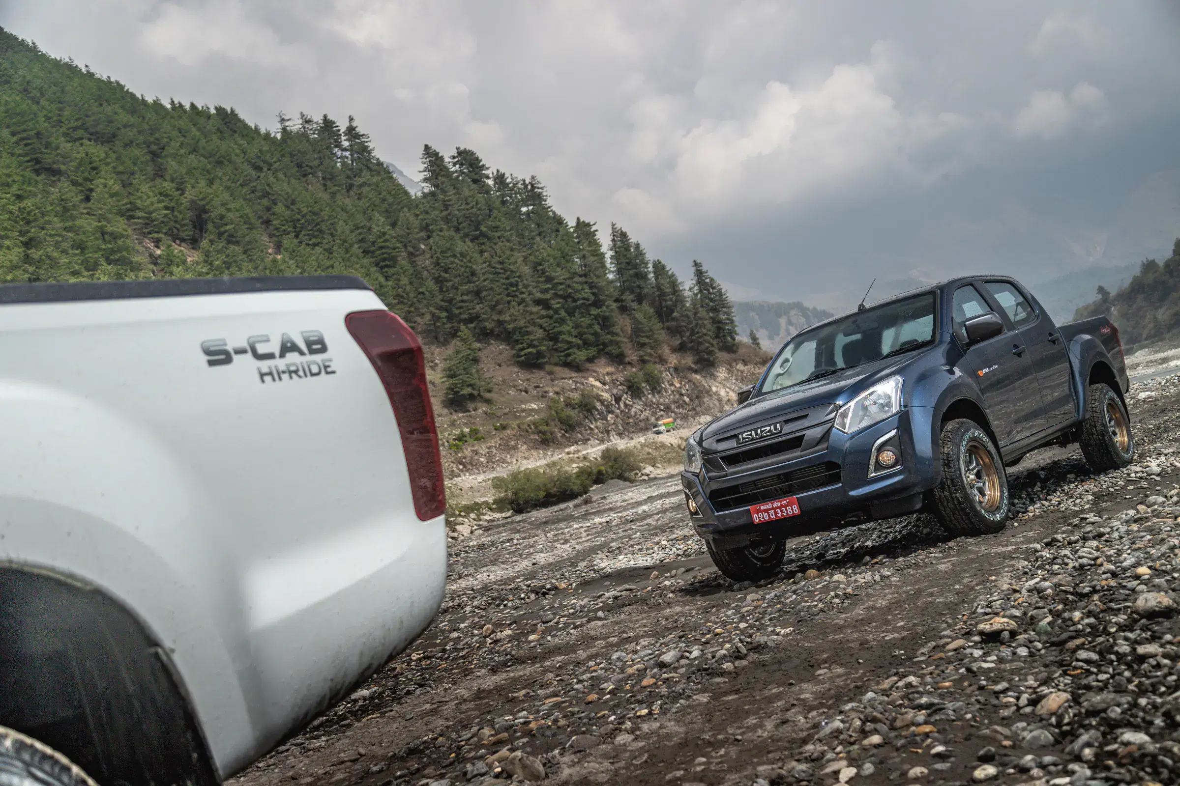 Outdoor vehicle scene featuring a vehicle, rocky terrain, a built structure, and cloudy sky.