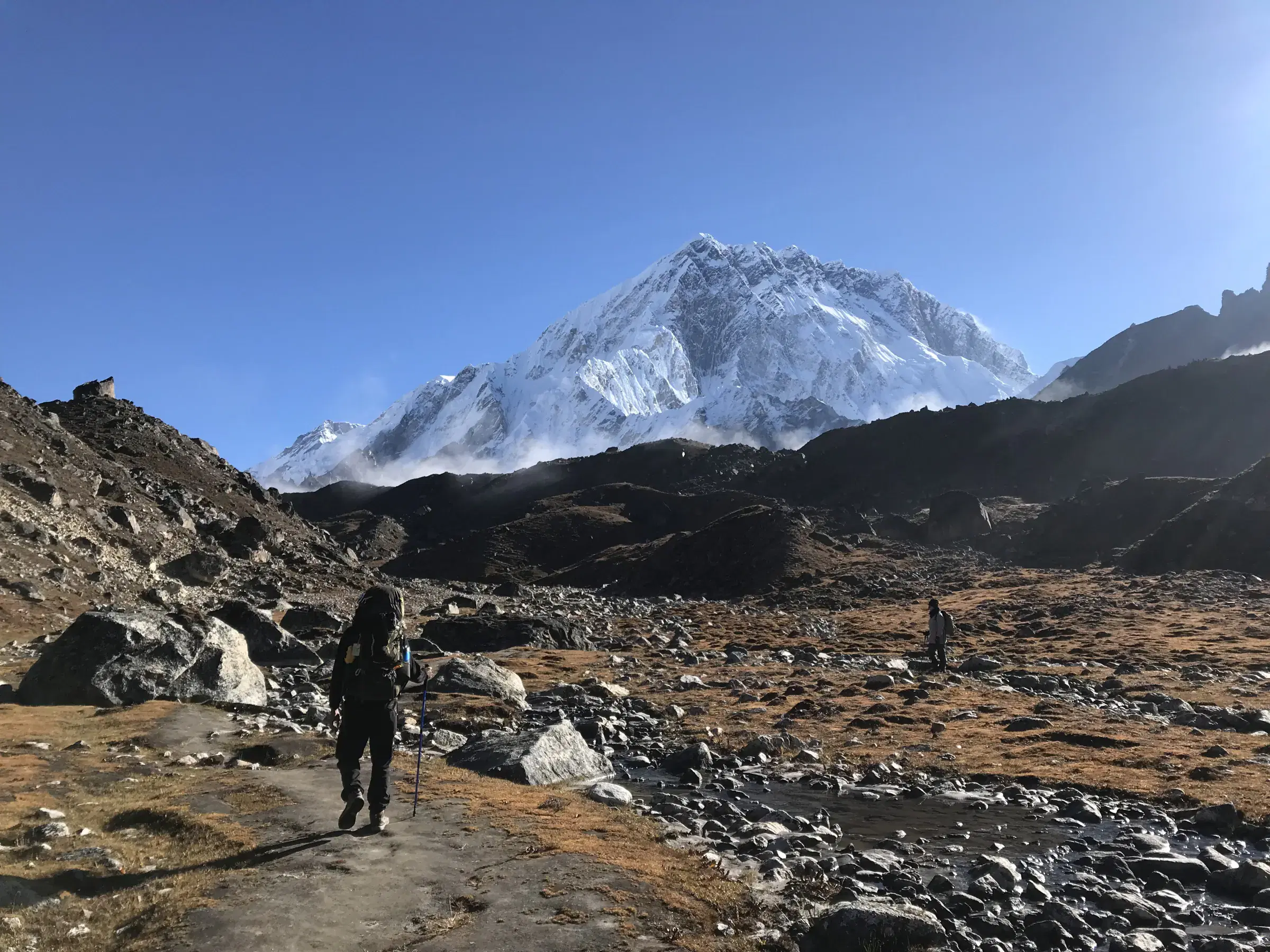 Outdoor scene featuring people, snowy terrain, a built structure, and blue sky.