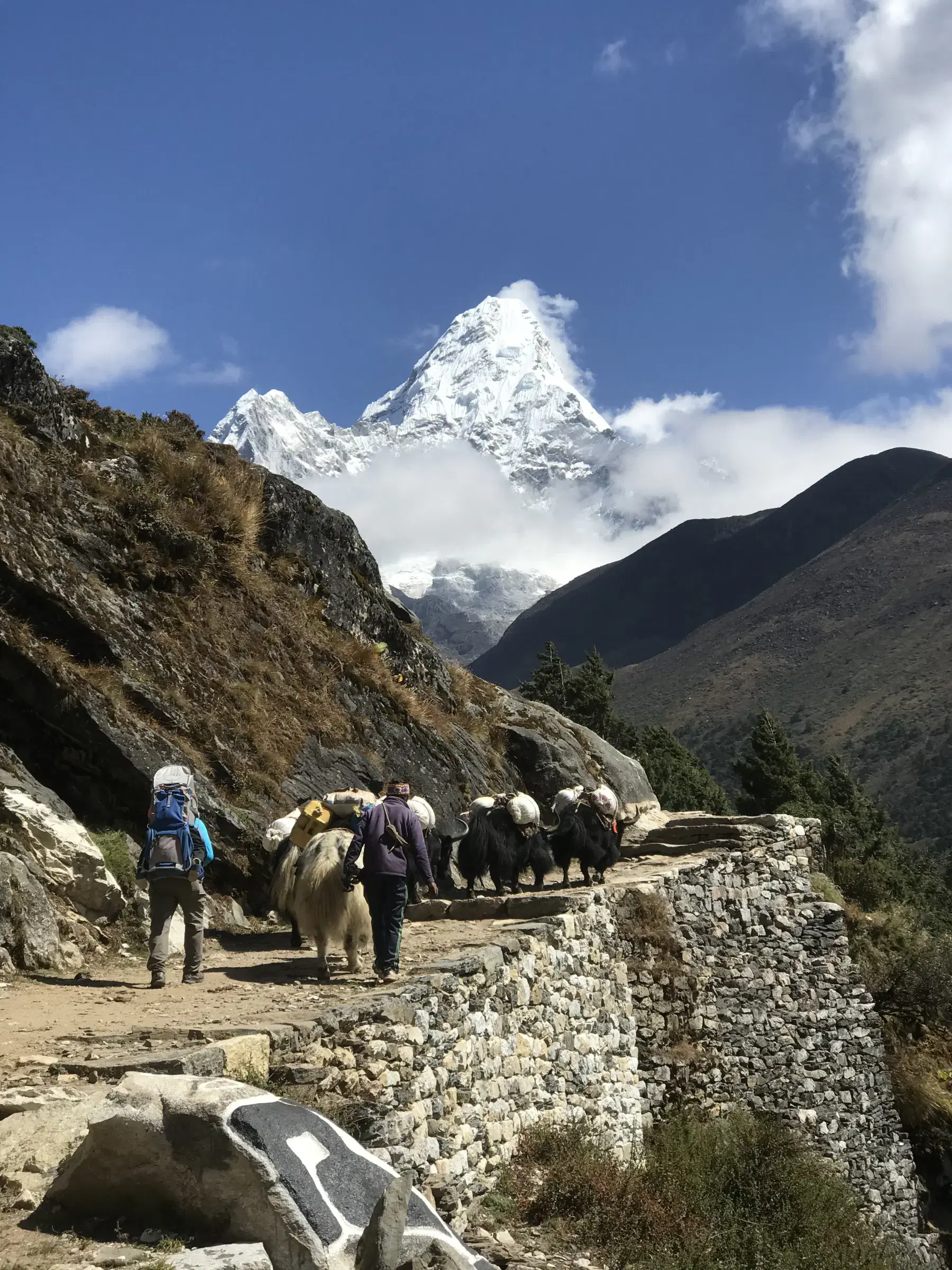 Outdoor scene featuring people, rocky terrain, a built structure, and cloudy sky.