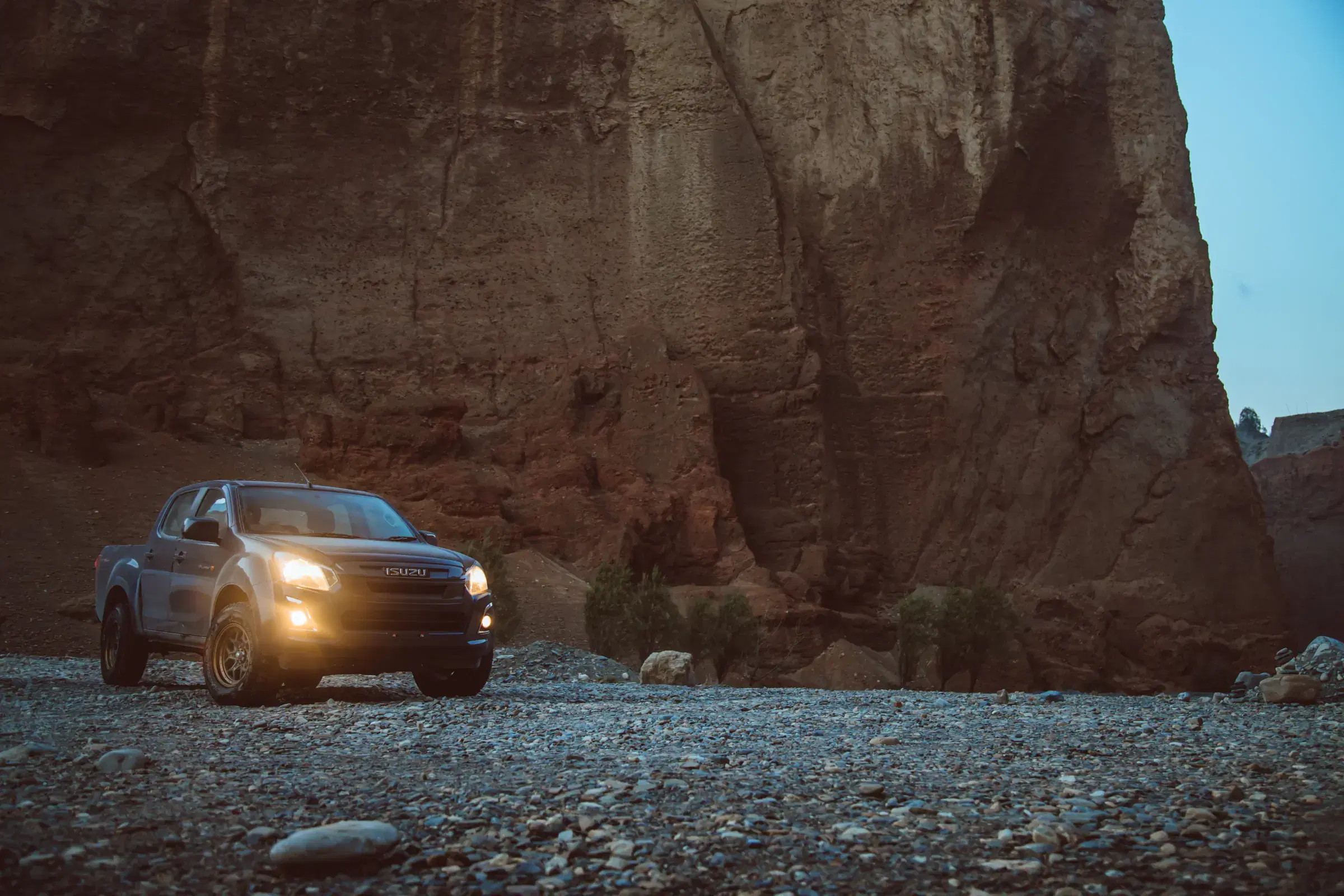 Outdoor vehicle scene featuring a vehicle, rocky terrain, a built structure, and blue sky.