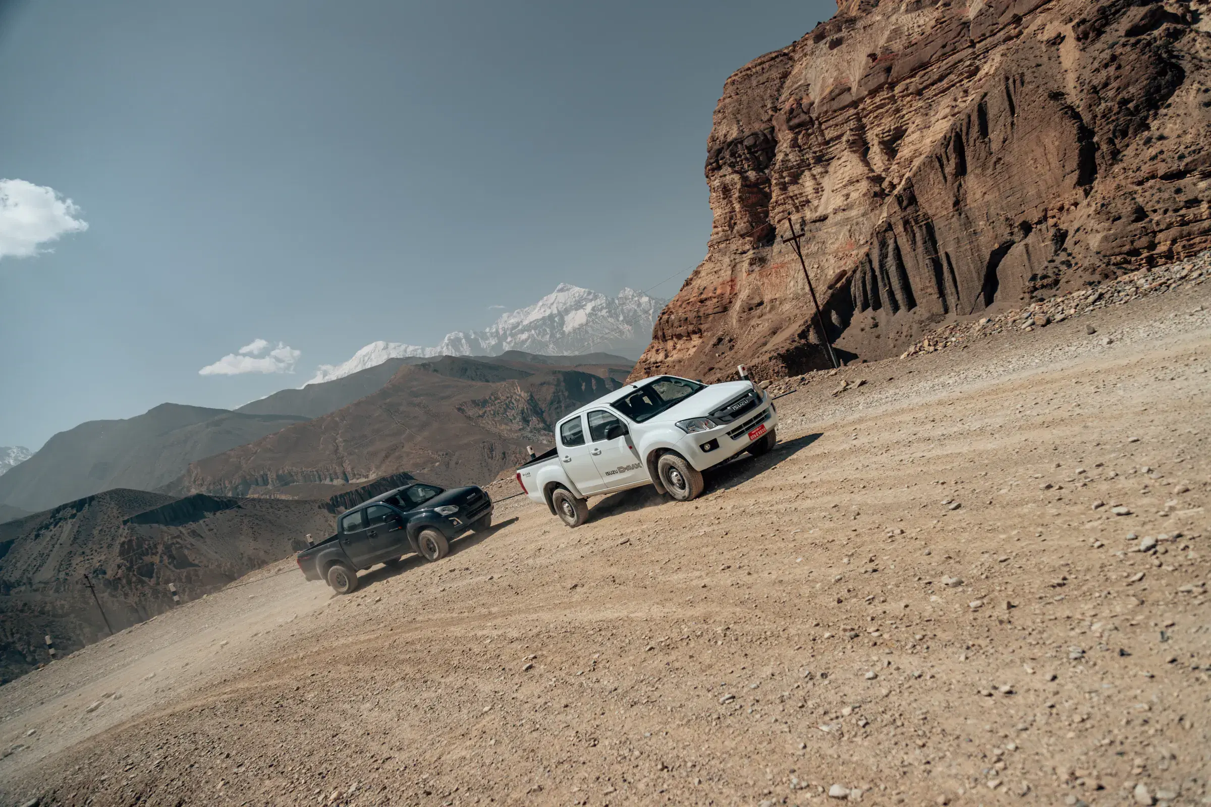 Outdoor vehicle scene featuring a vehicle, rocky terrain, a built structure, and cloudy sky.