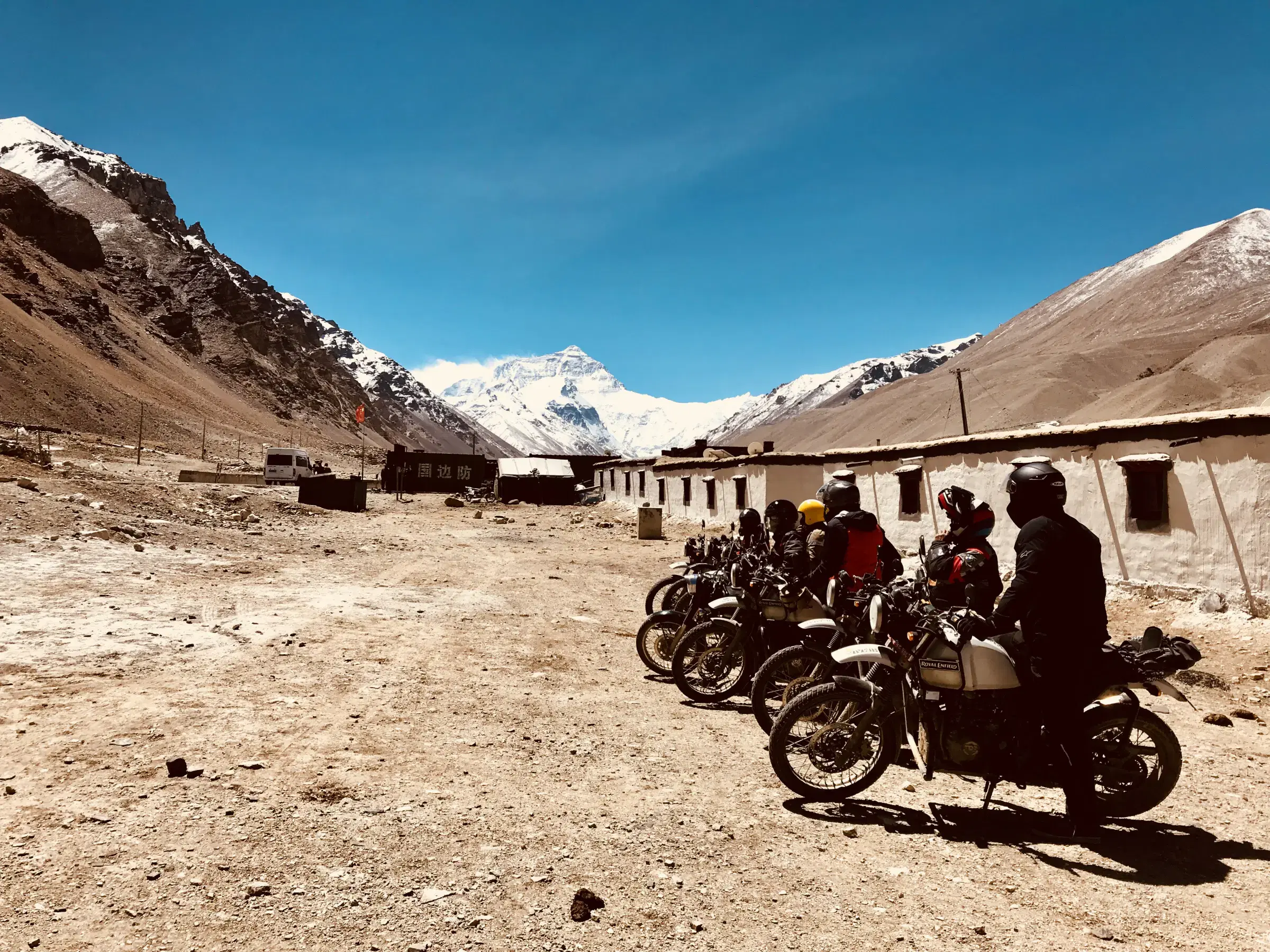 Outdoor scene featuring people, rocky terrain, a built structure, and blue sky.