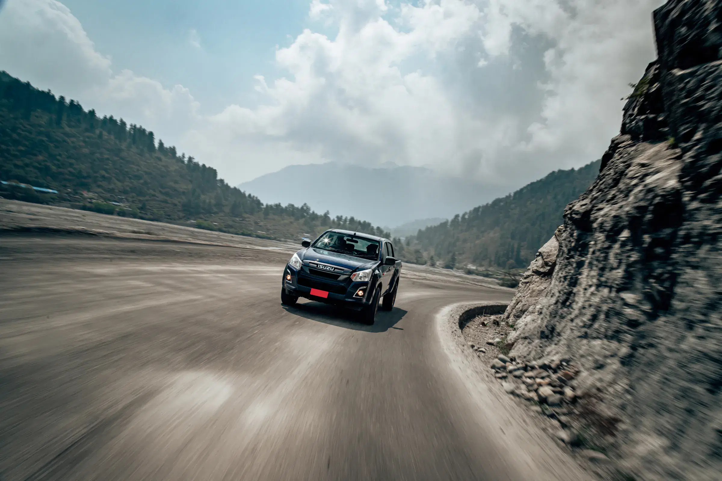 Outdoor vehicle scene featuring a vehicle, rocky terrain, a built structure, and cloudy sky.
