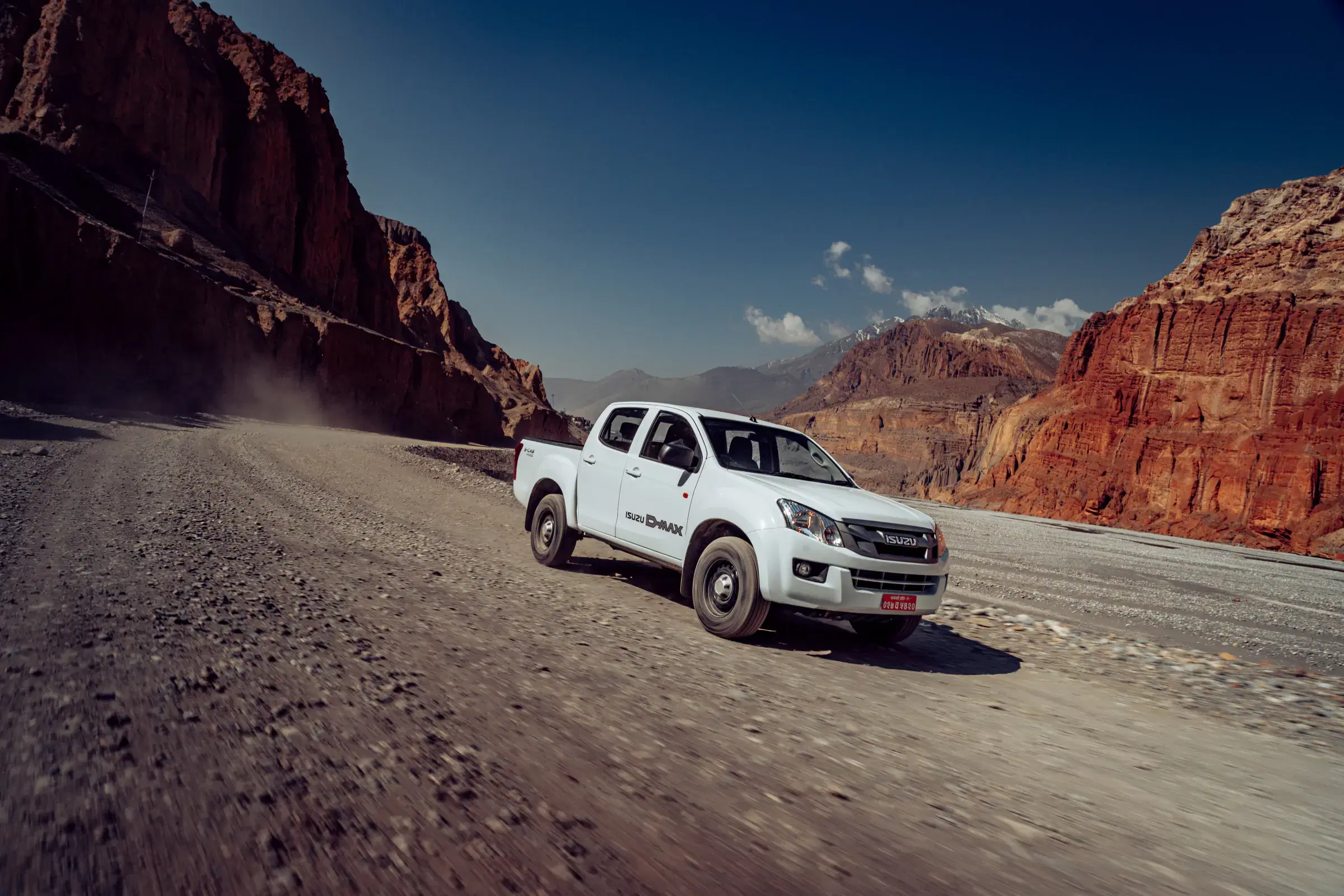 Outdoor vehicle scene featuring a vehicle, rocky terrain, a built structure, and blue sky.