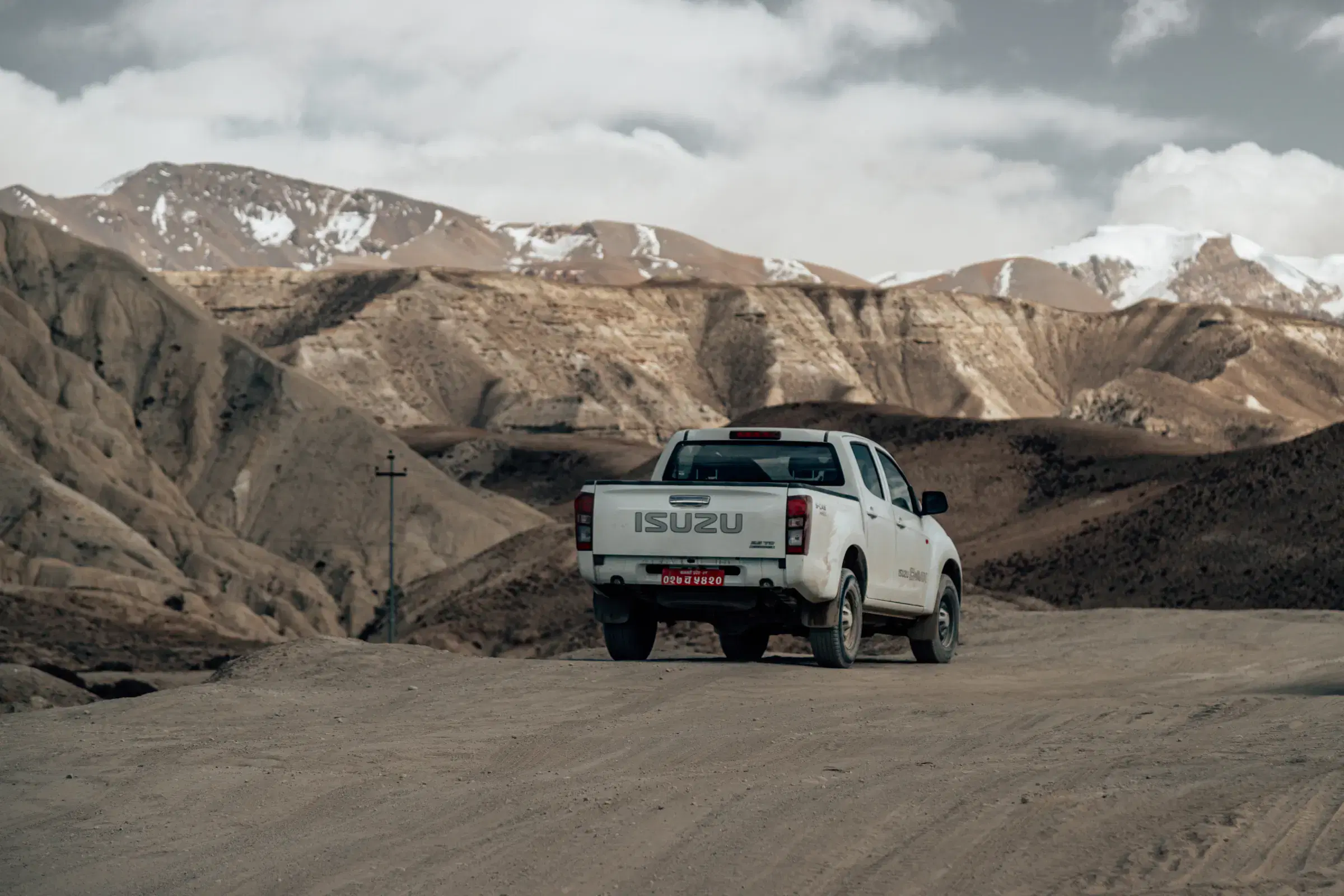 Outdoor vehicle scene featuring a vehicle, rocky terrain, a built structure, and cloudy sky.