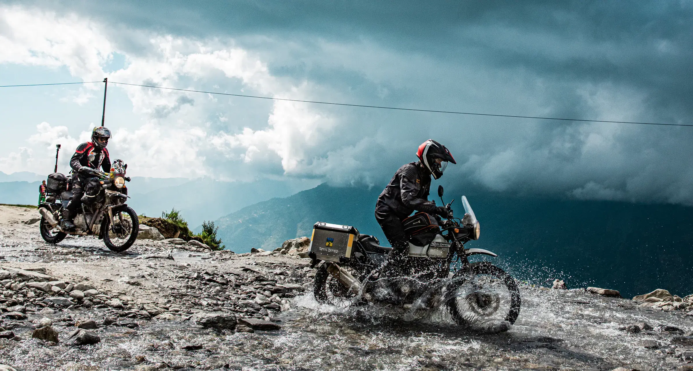 Outdoor scene featuring people, rocky terrain, a built structure, and cloudy sky.