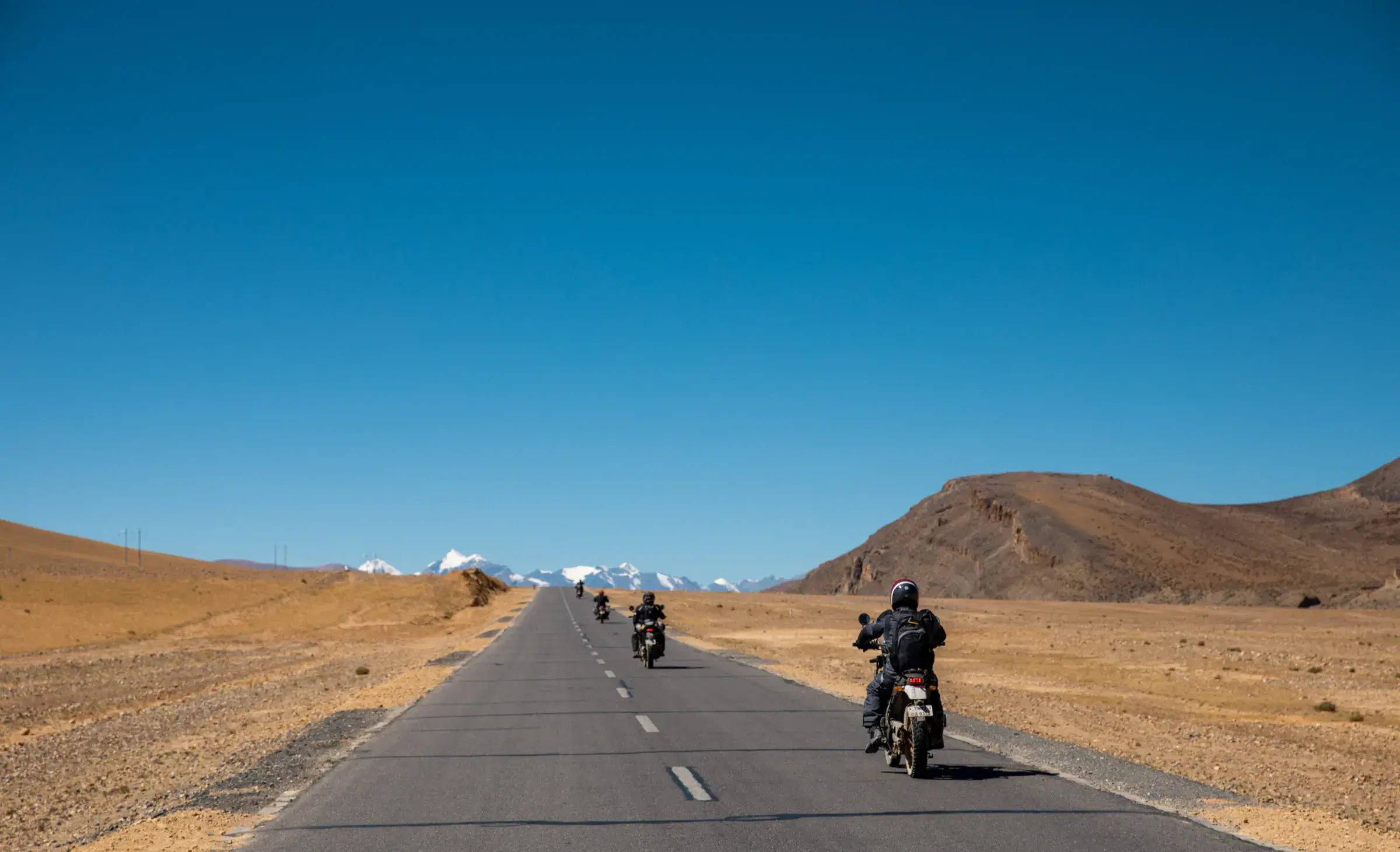 Outdoor adventure scene featuring people, a vehicle, rocky terrain, and blue sky.