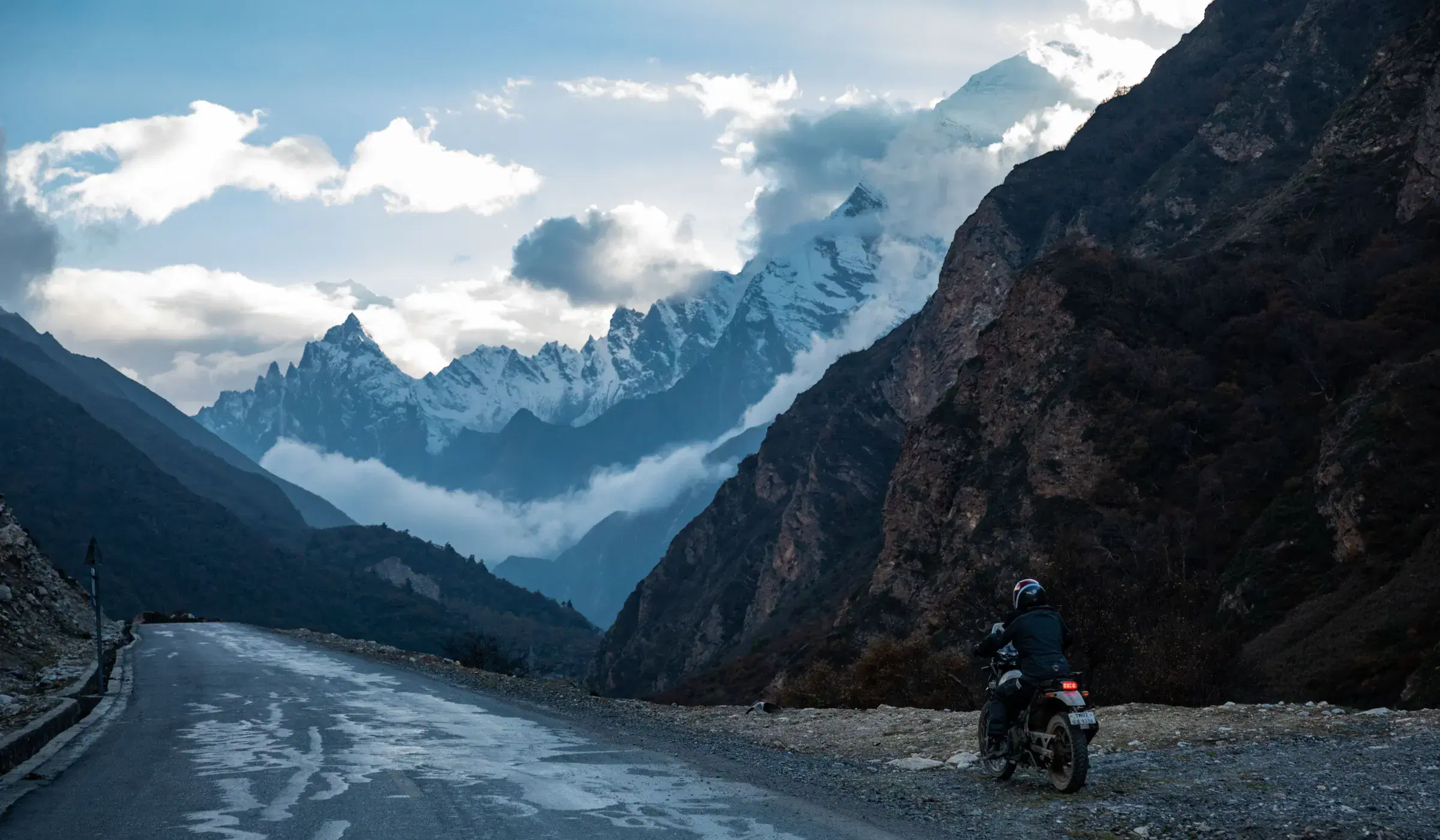 Mountain landscape featuring rocky terrain, water, a built structure, and cloudy sky.