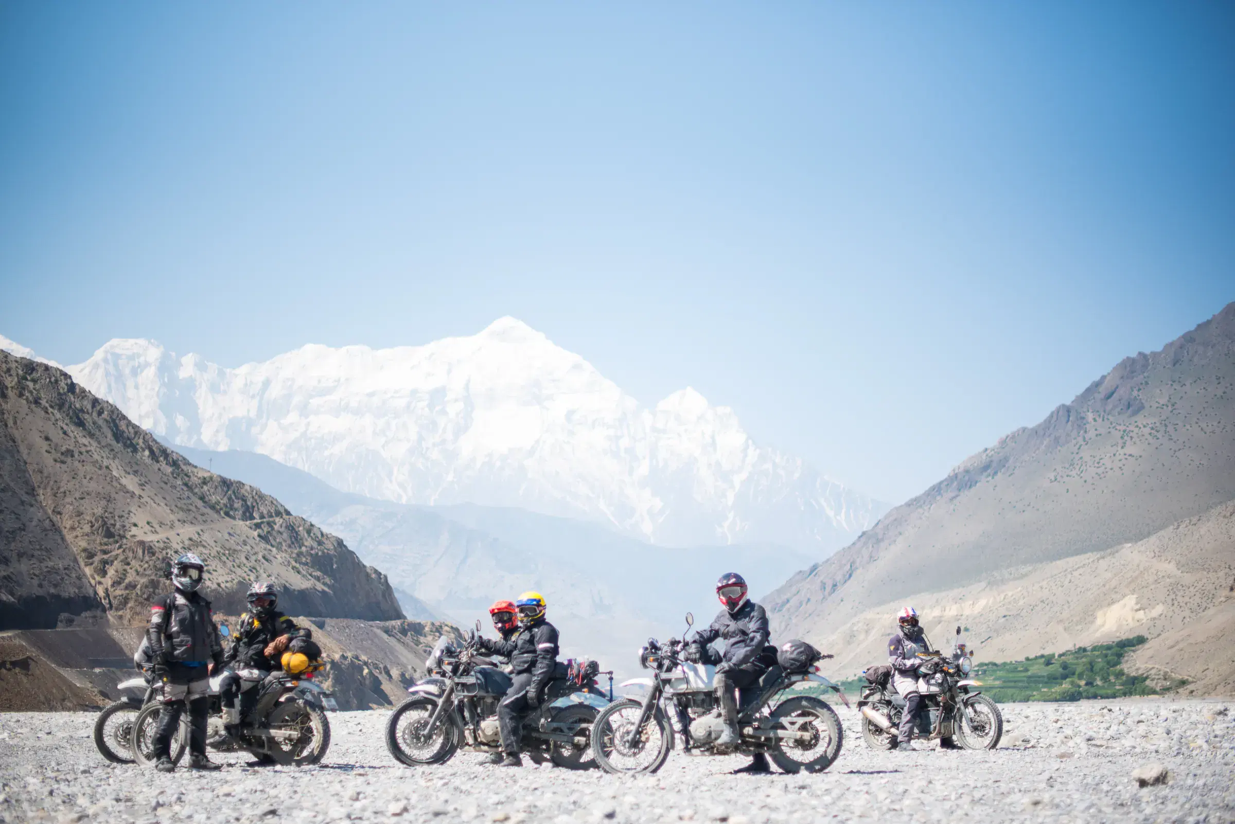 Outdoor scene featuring people, snowy terrain, water, and blue sky.