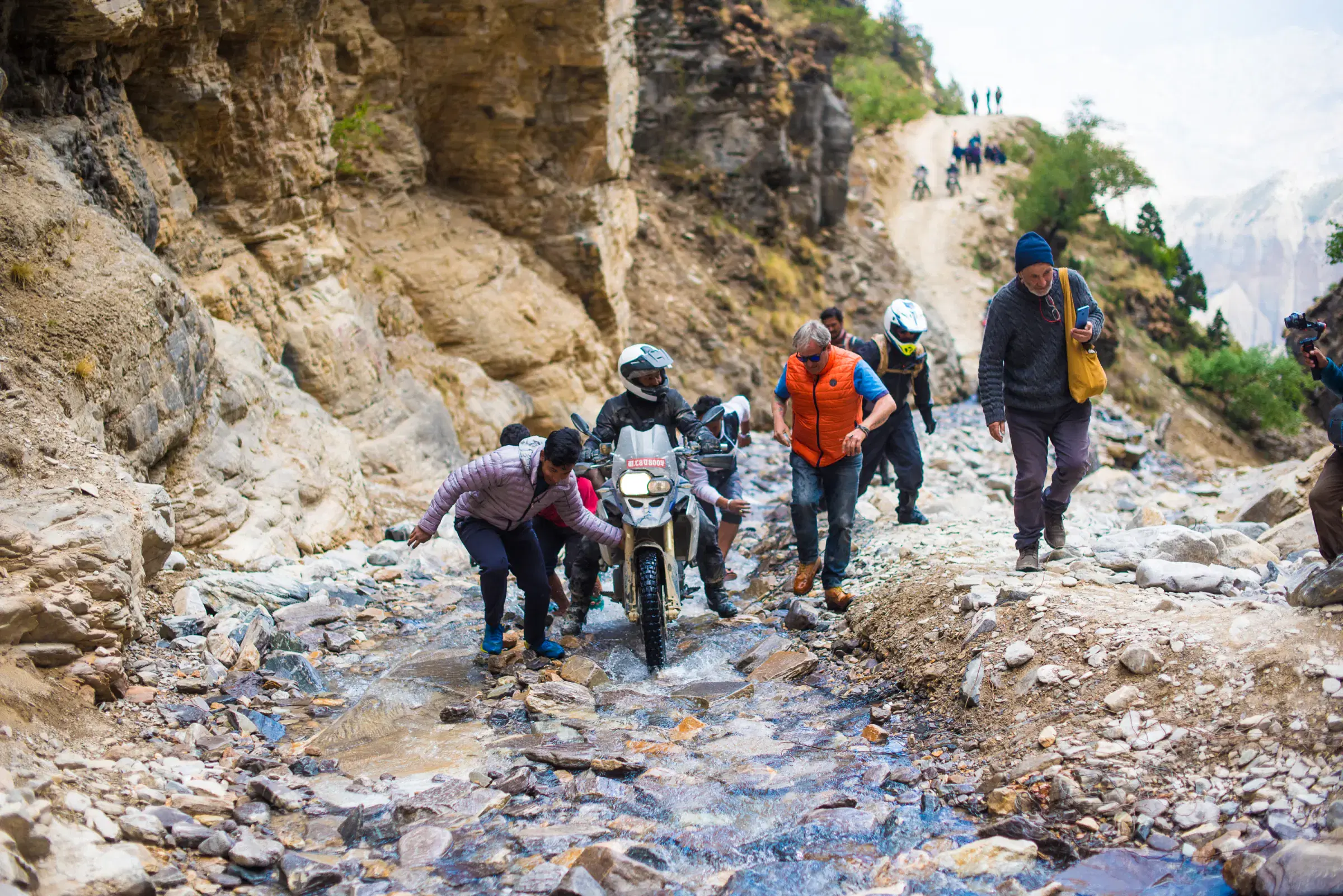 Outdoor scene featuring people, rocky terrain, and a built structure.
