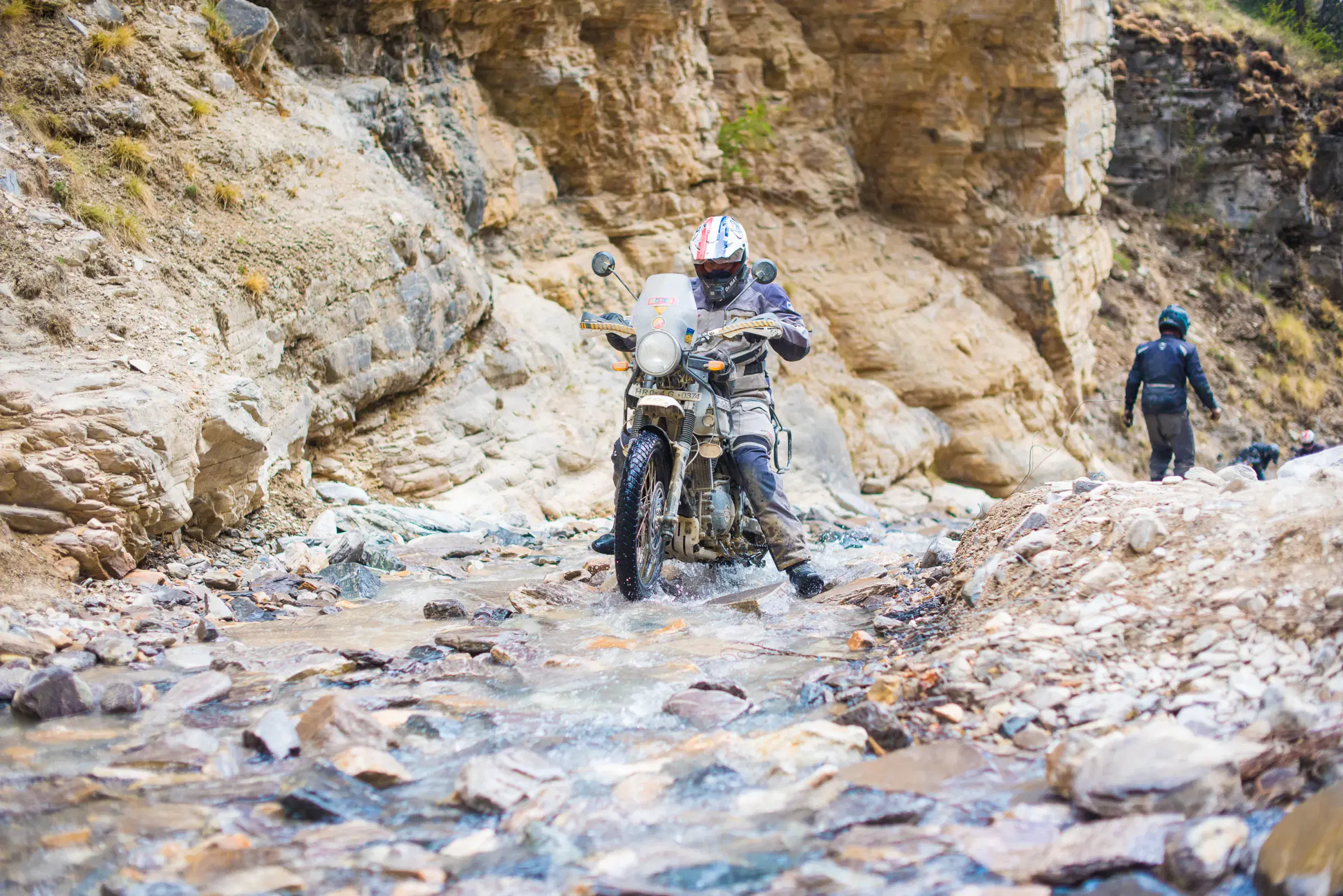 Outdoor adventure scene featuring people, a vehicle, rocky terrain, and a built structure.