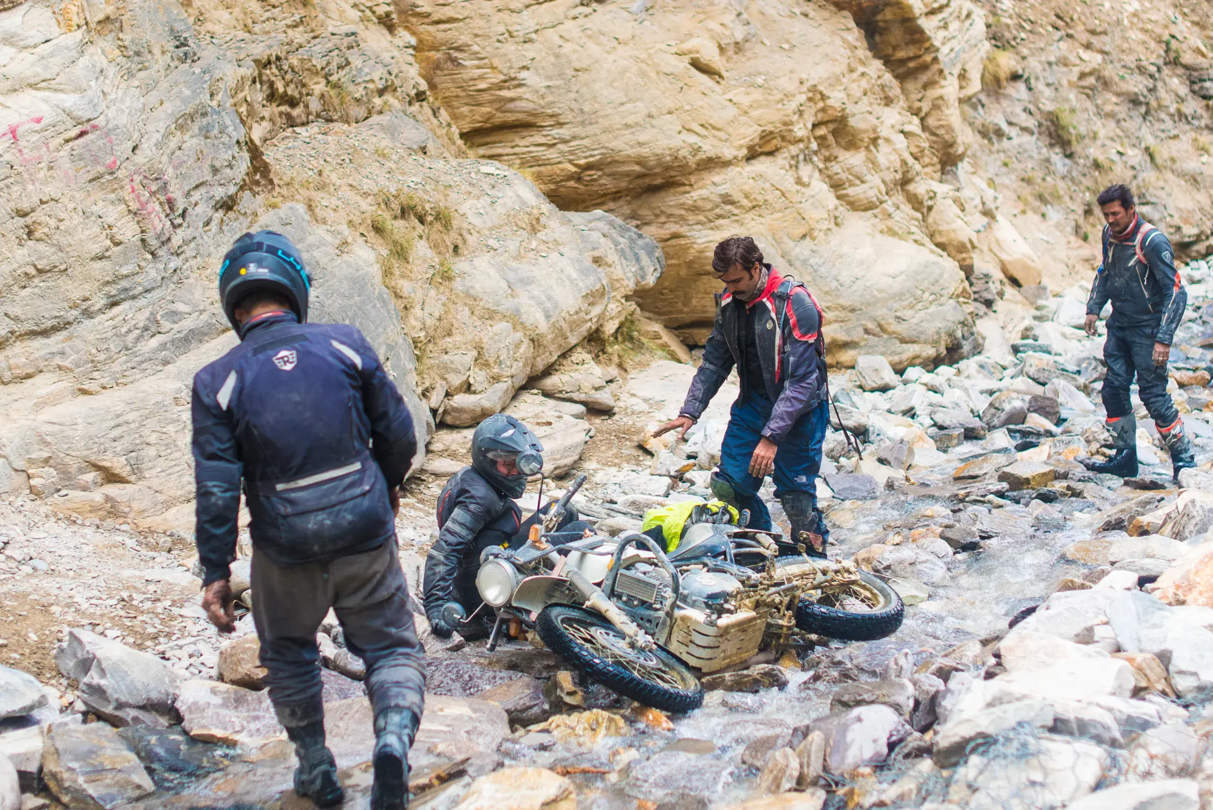 Outdoor scene featuring people, rocky terrain, and a built structure.