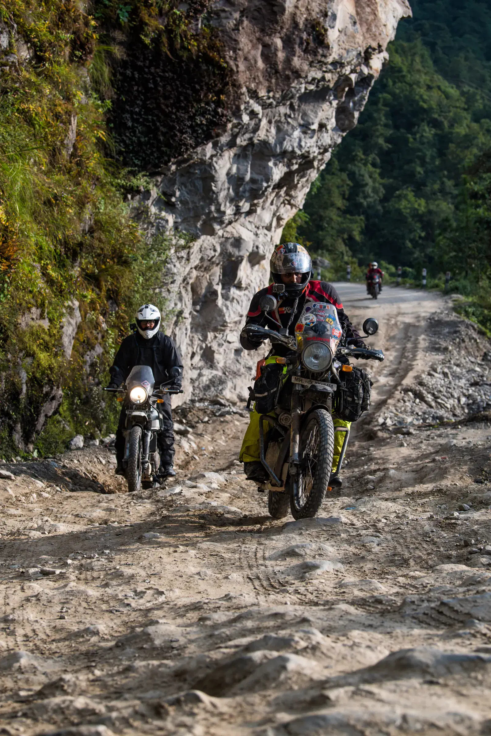 Portrait-oriented Outdoor adventure scene featuring people, a vehicle, rocky terrain, and a built structure.