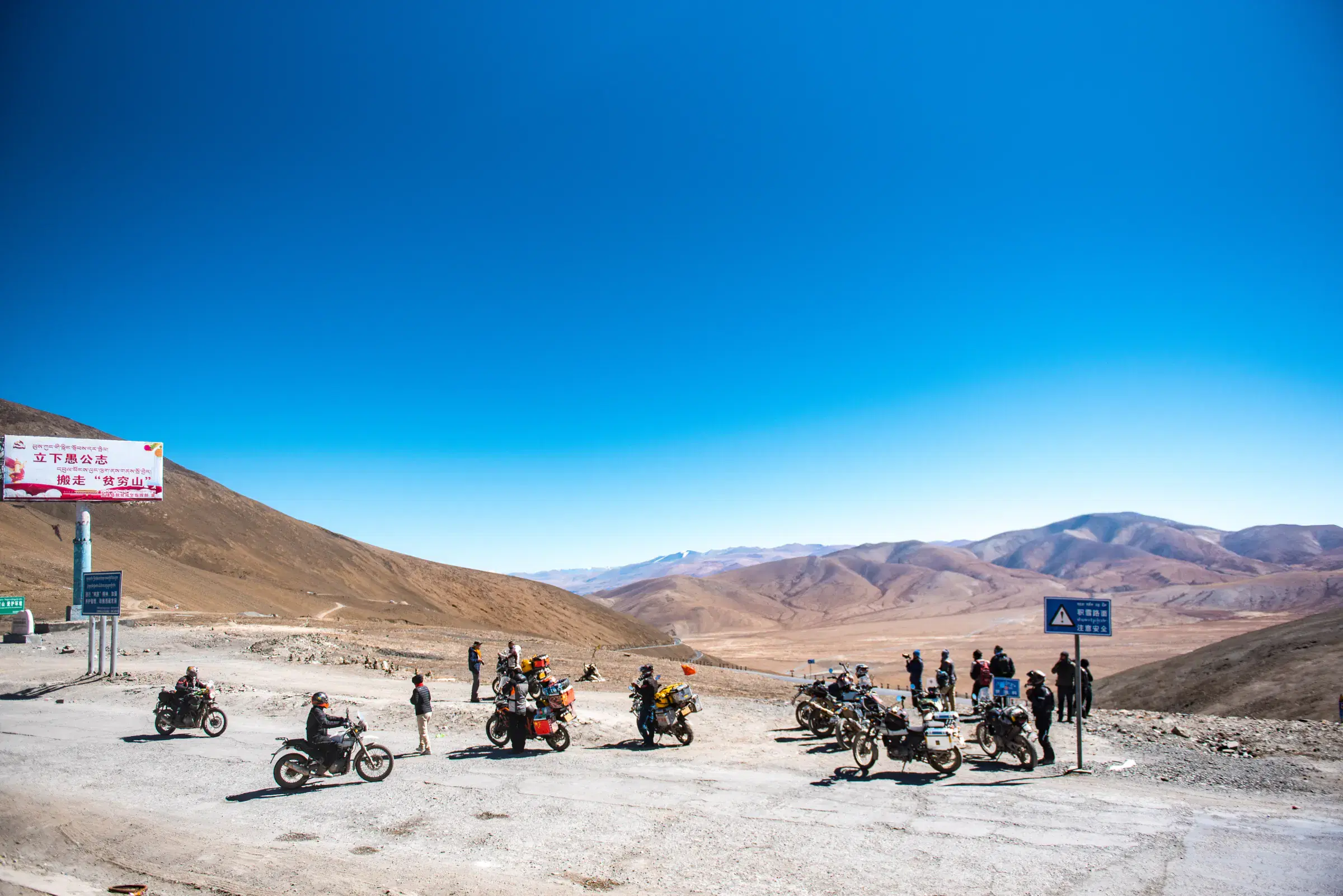 Outdoor adventure scene featuring people, a vehicle, rocky terrain, and blue sky.