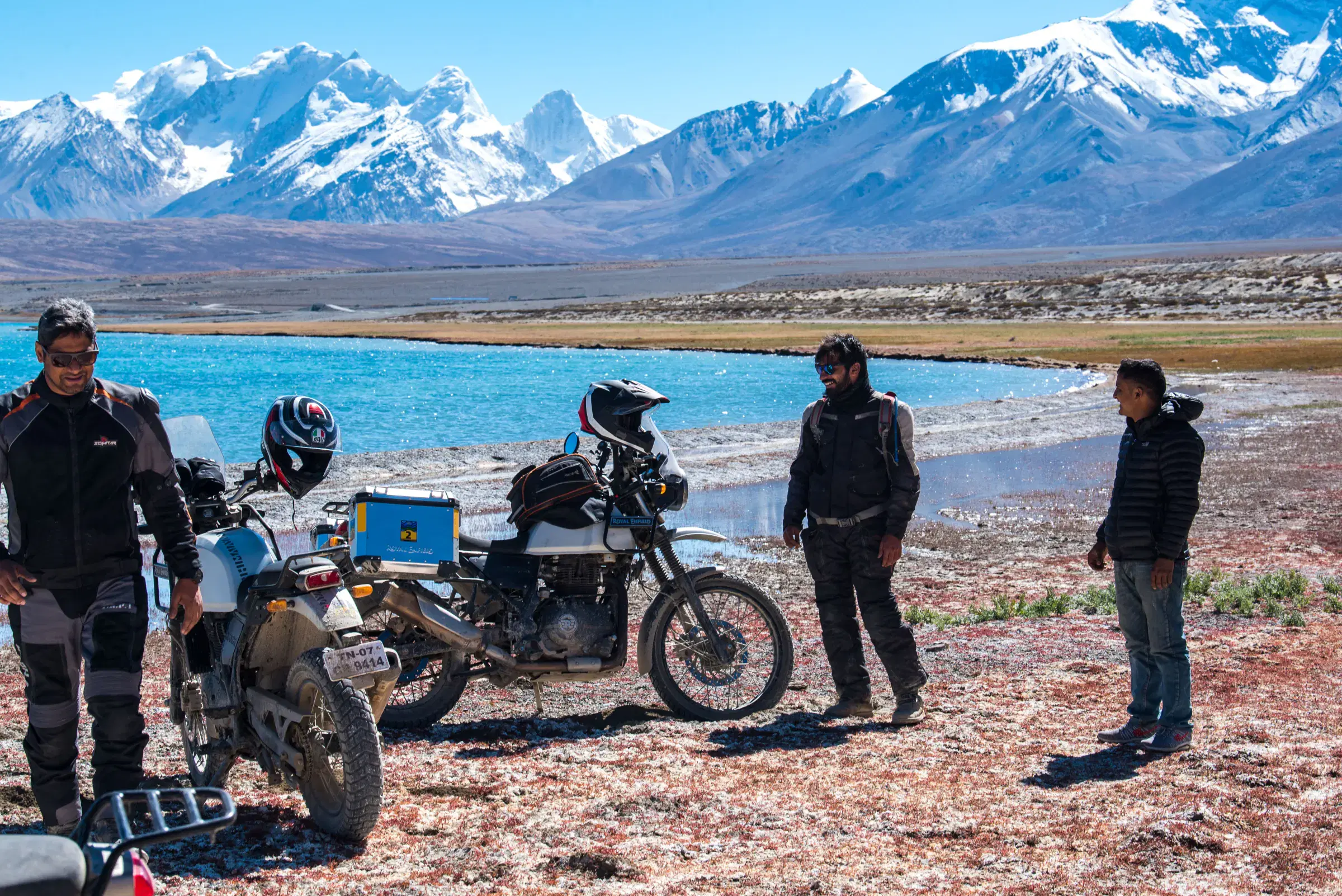 Outdoor scene featuring people, snowy terrain, water, and blue sky.