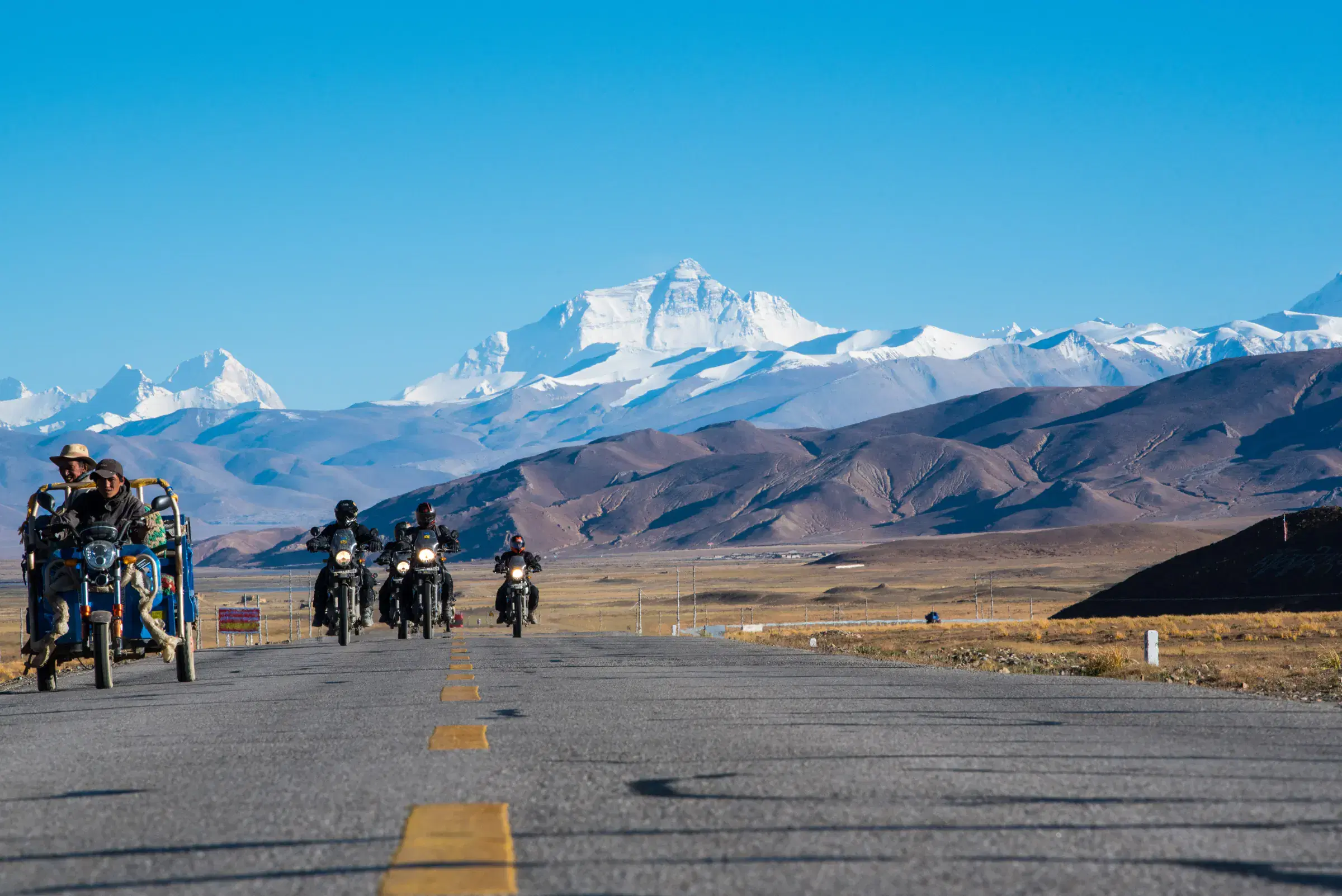 Outdoor scene featuring people, snowy terrain, water, and blue sky.