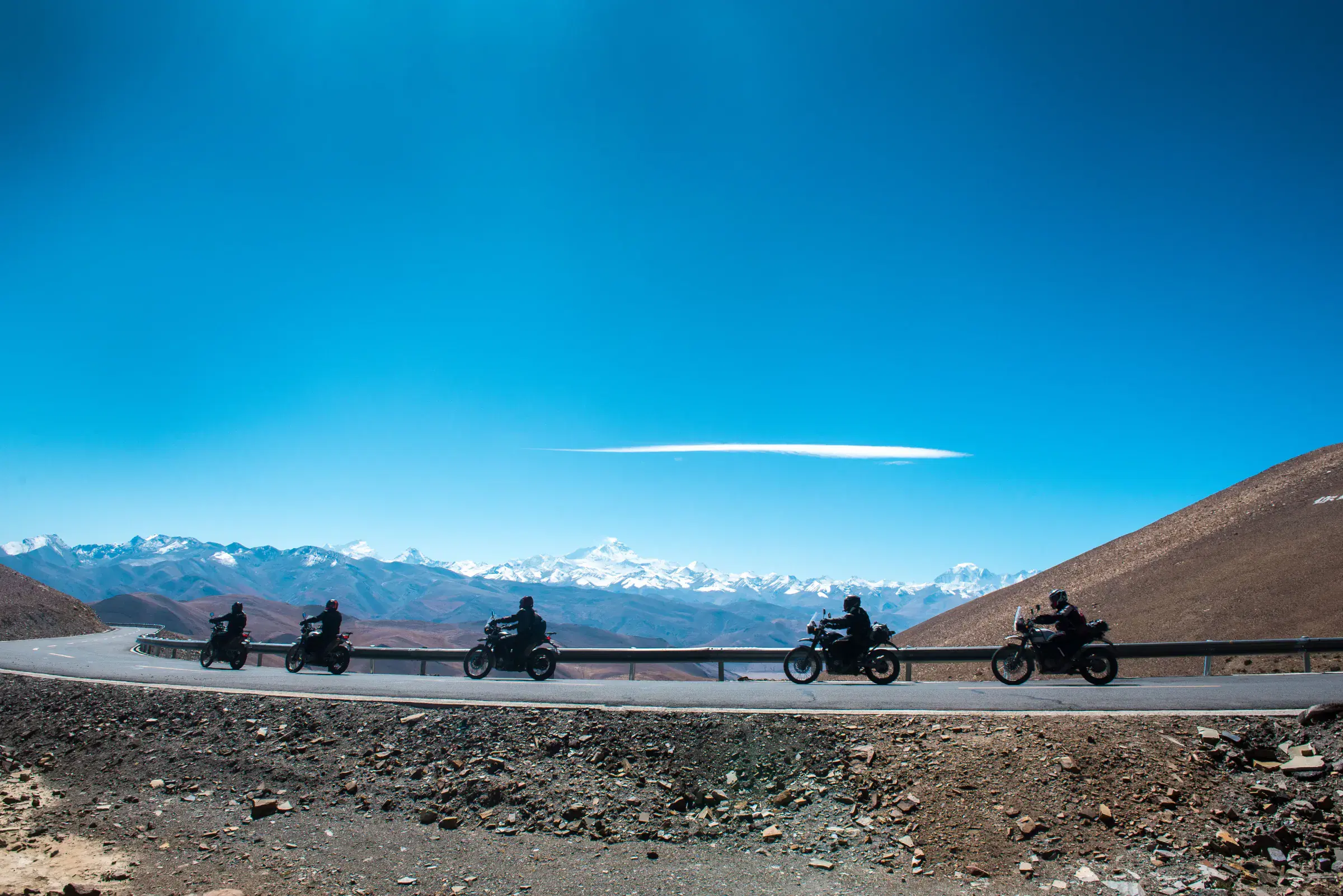 Mountain landscape featuring rocky terrain, water, a built structure, and blue sky.