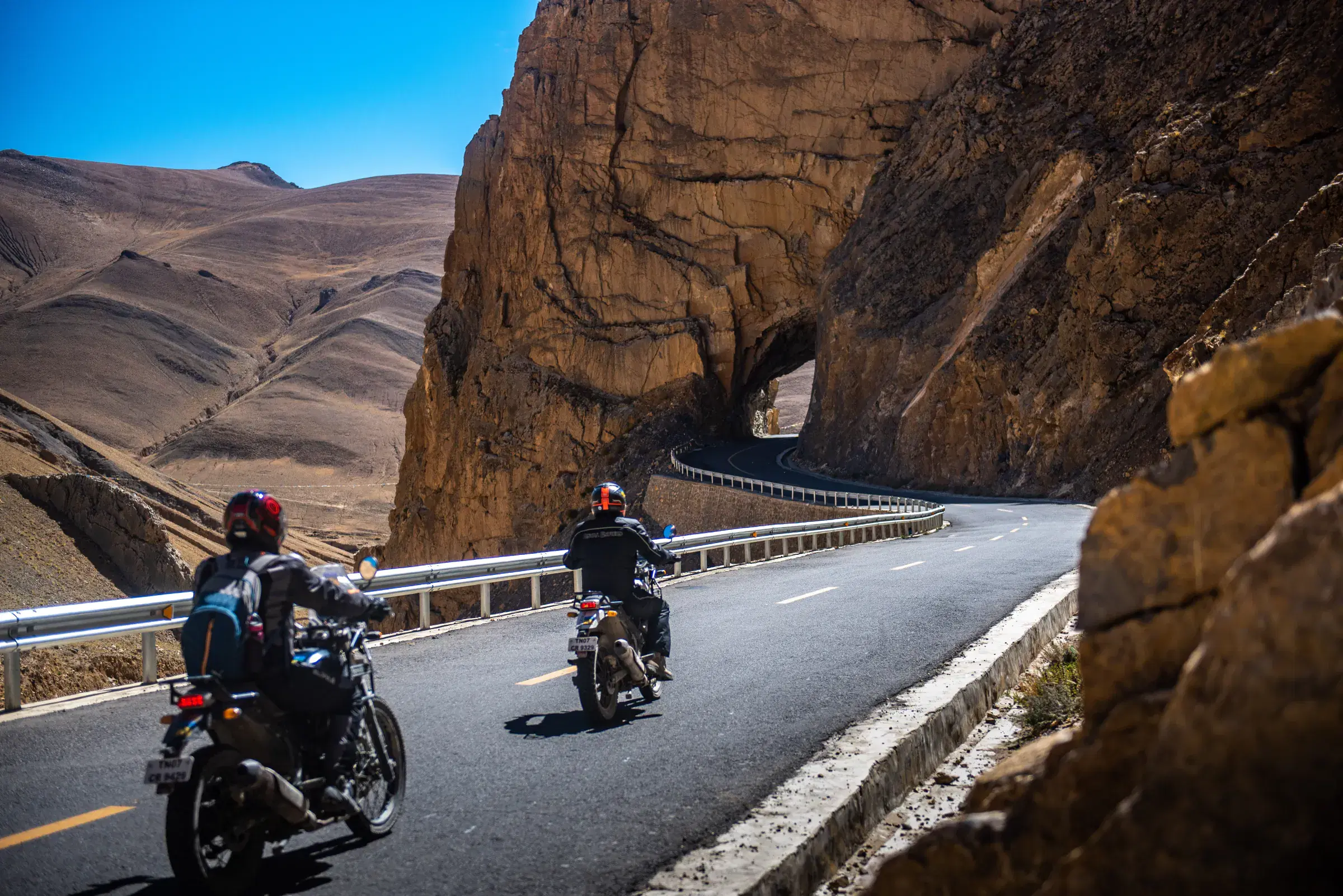 Outdoor adventure scene featuring people, a vehicle, rocky terrain, a built structure, and blue sky.