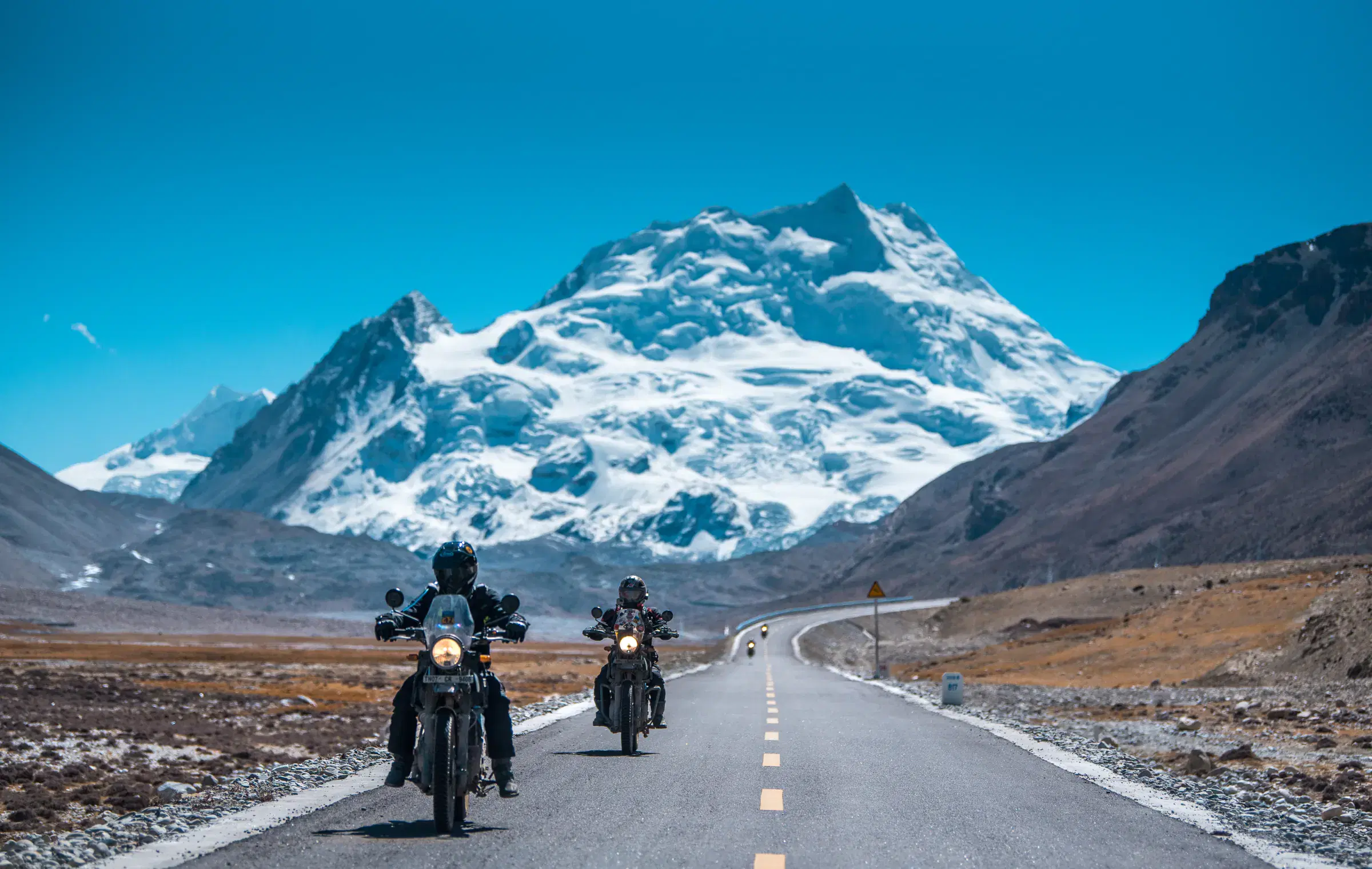 Outdoor scene featuring people, snowy terrain, water, and blue sky.