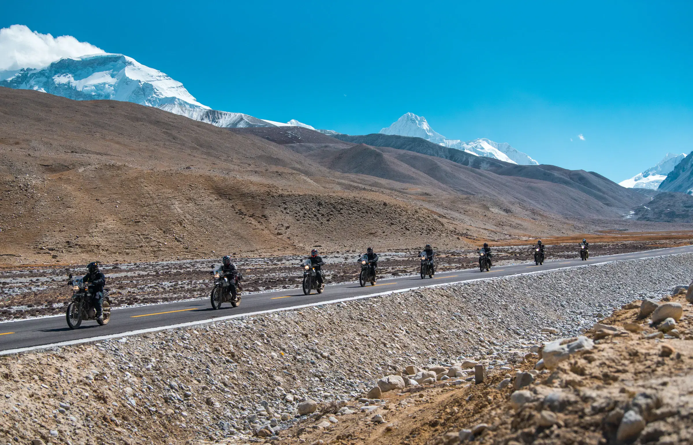 Mountain landscape featuring snowy terrain, water, a built structure, and blue sky.