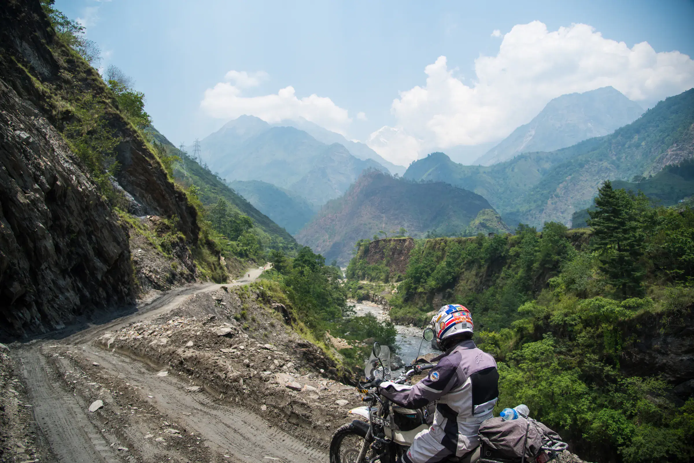 Outdoor scene featuring people, rocky terrain, a built structure, and cloudy sky.
