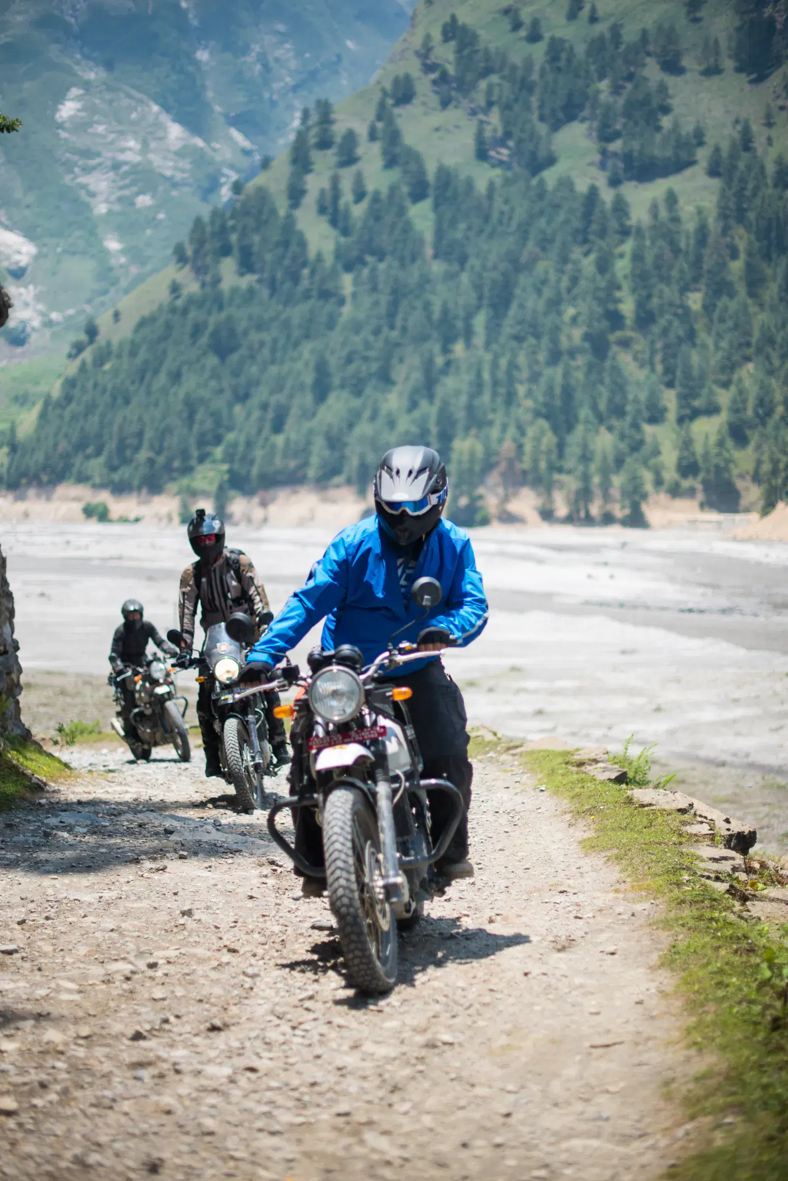 Portrait-oriented Outdoor adventure scene featuring people, a vehicle, rocky terrain, and greenery.