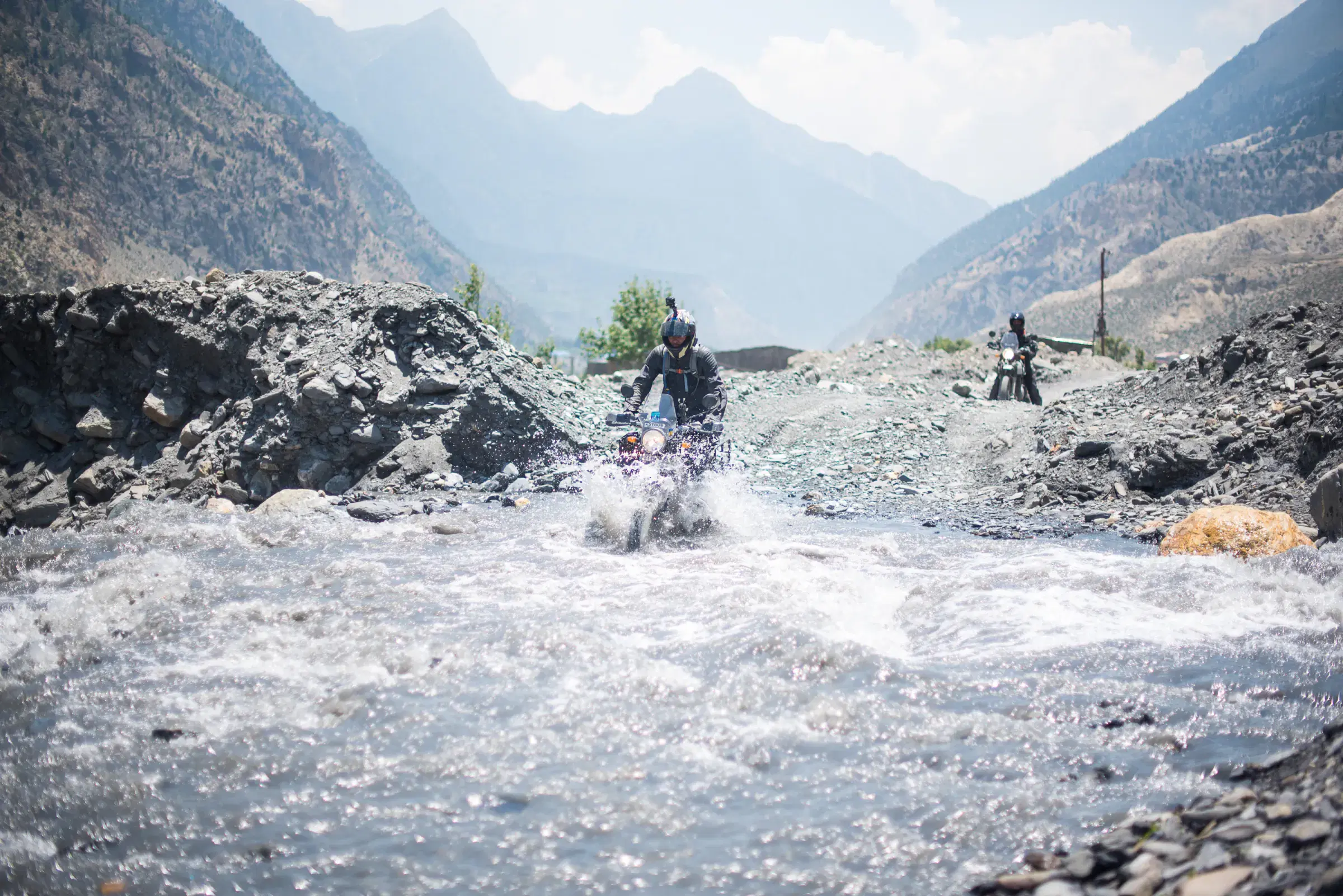 Outdoor scene featuring people, rocky terrain, a built structure, and cloudy sky.