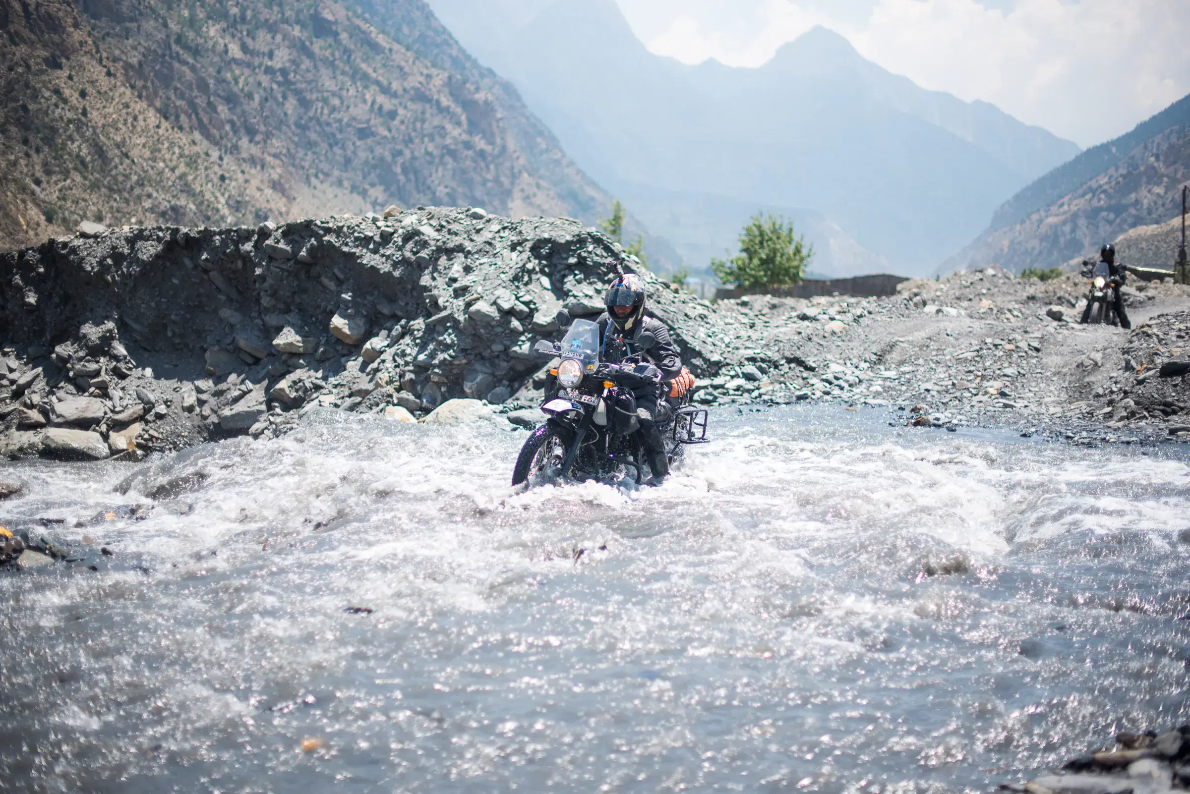 Outdoor scene featuring people, rocky terrain, a built structure, and cloudy sky.