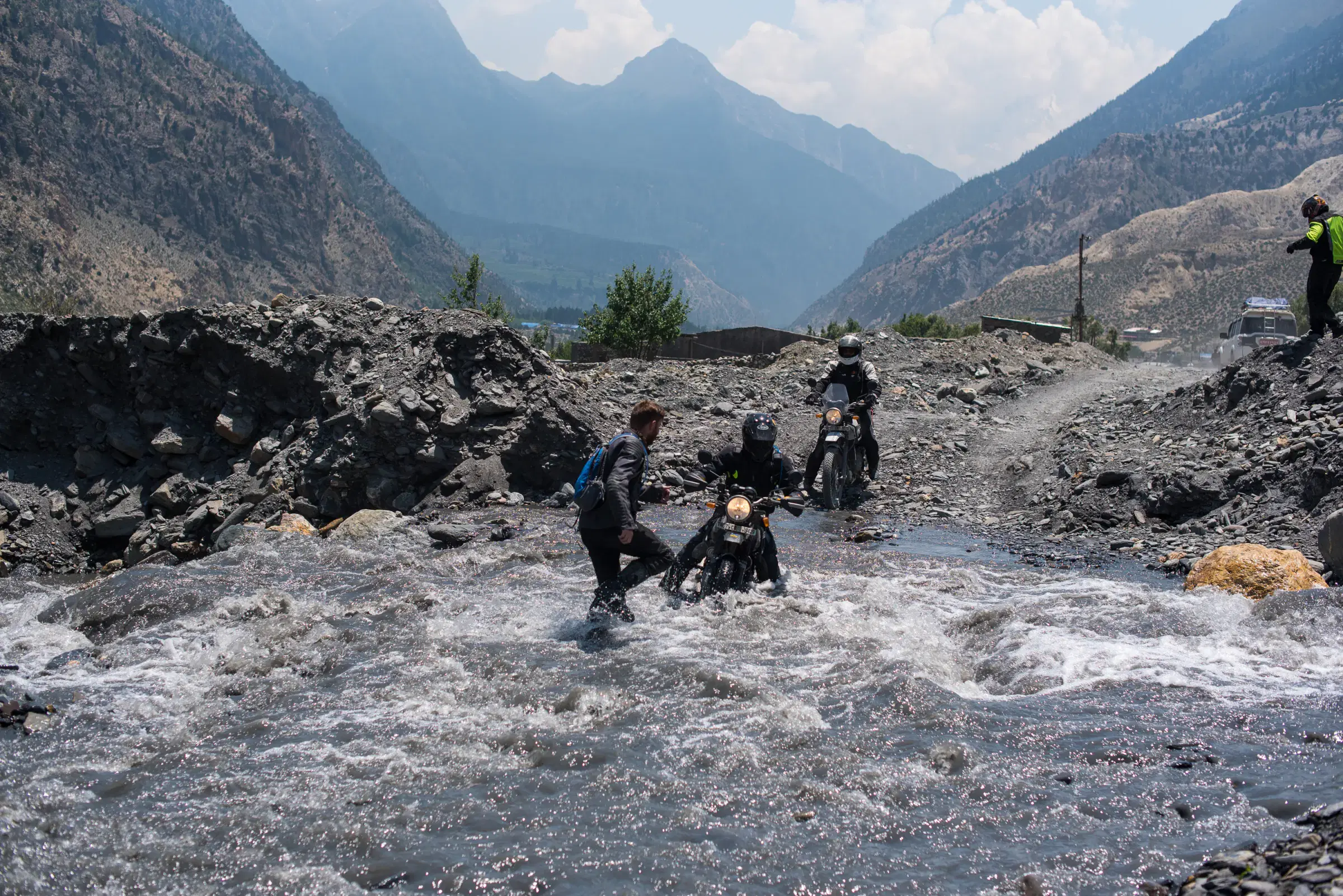 Outdoor scene featuring people, rocky terrain, a built structure, and cloudy sky.